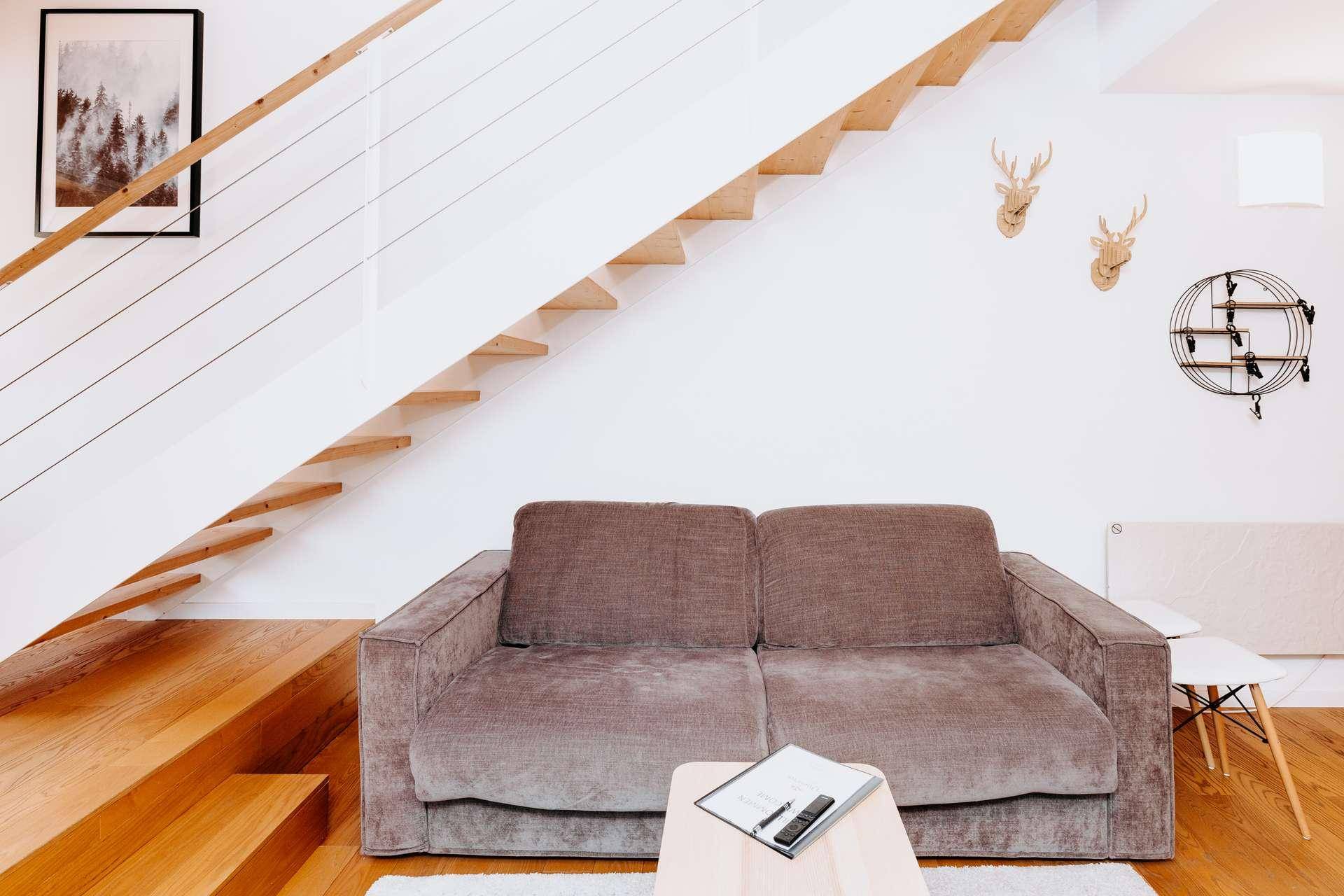 Gemütlicher Wohnbereich mit Sofa, Holzboden und offener Holztreppe.