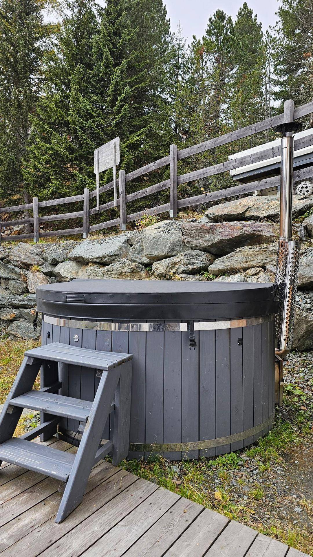 Außenwhirlpool auf einer Holzterrasse, umgeben von Natur und Bäumen.