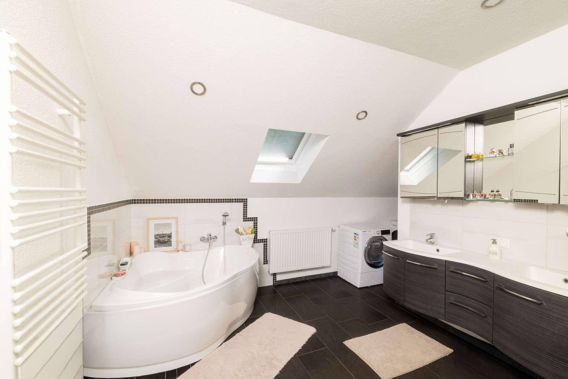Geräumiges Badezimmer mit Eckbadewanne, Waschmaschine und Dachfenster unter der Schräge.