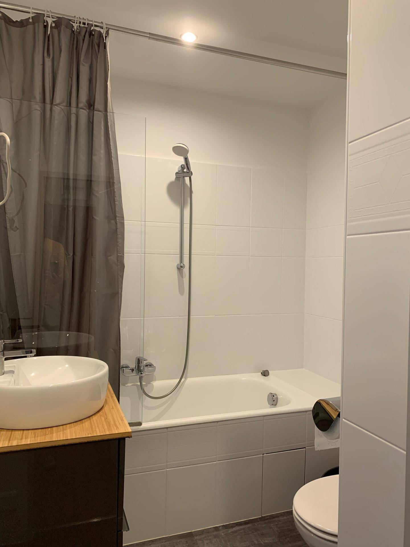 Helles Badezimmer mit Badewanne, Duschvorhang und modernem Waschbecken.