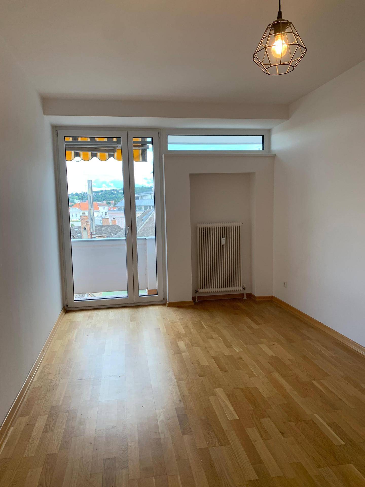Leerer Raum mit Holzboden, Balkonzugang und Blick auf die Umgebung.