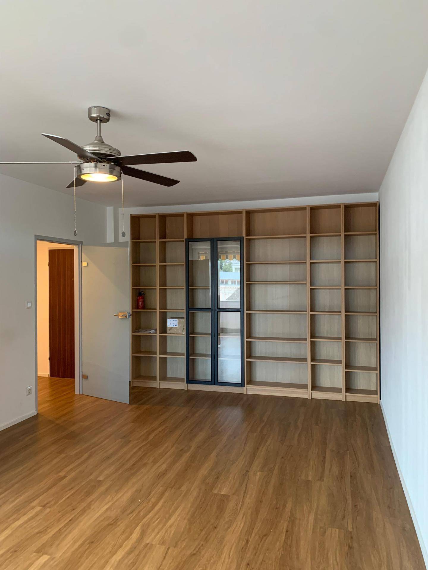 Geräumiger Raum mit Holzboden, Deckenventilator und großer Bücherwand.