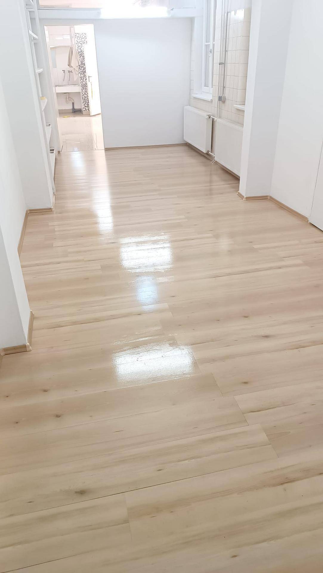 Leerer Raum mit glänzendem Holzboden und weißen Wänden, der auf einen weiteren Bereich führt.