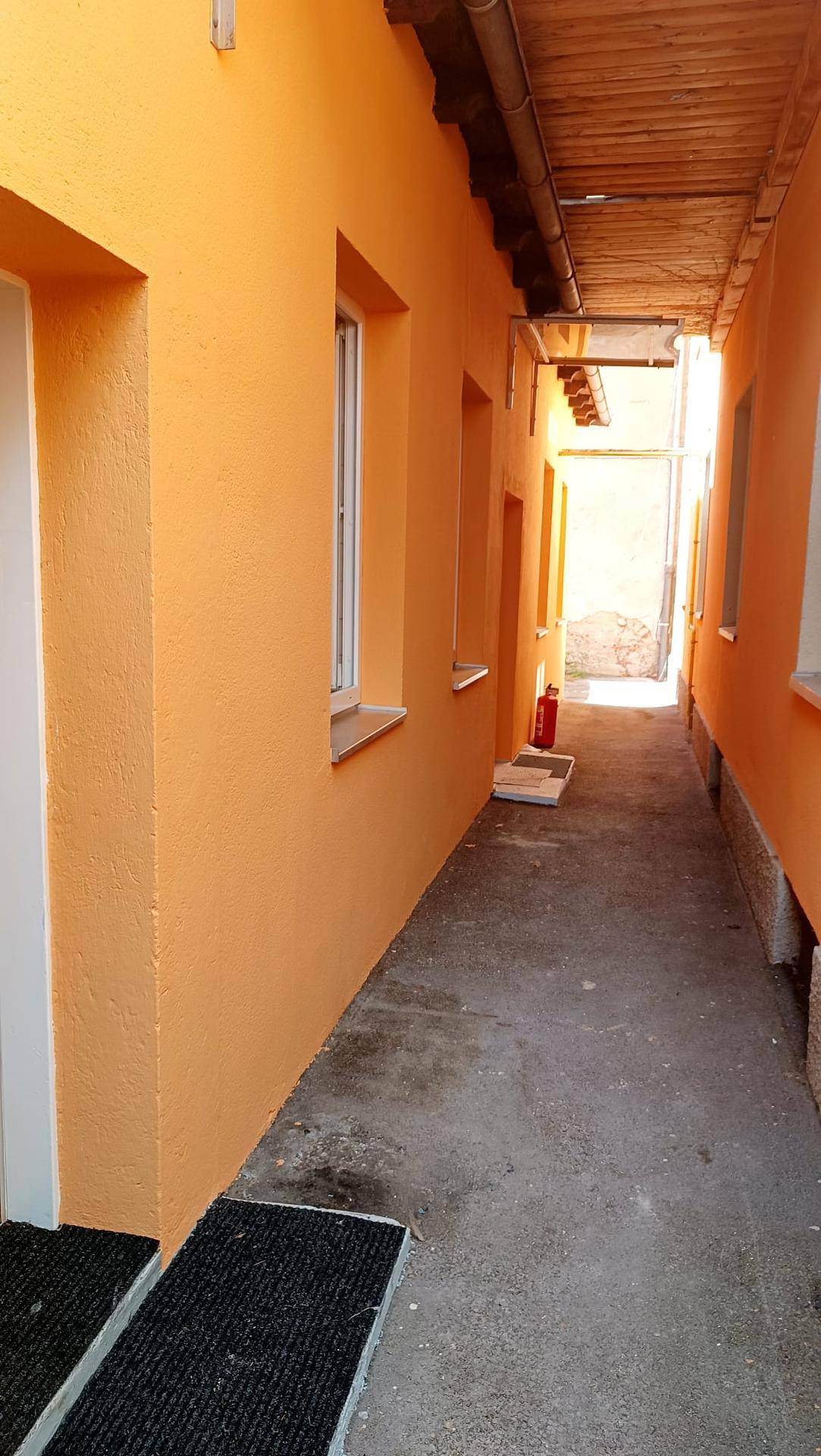 Schmaler Durchgang zwischen Gebäuden mit orangefarbenen Wänden und einem Holzdach.