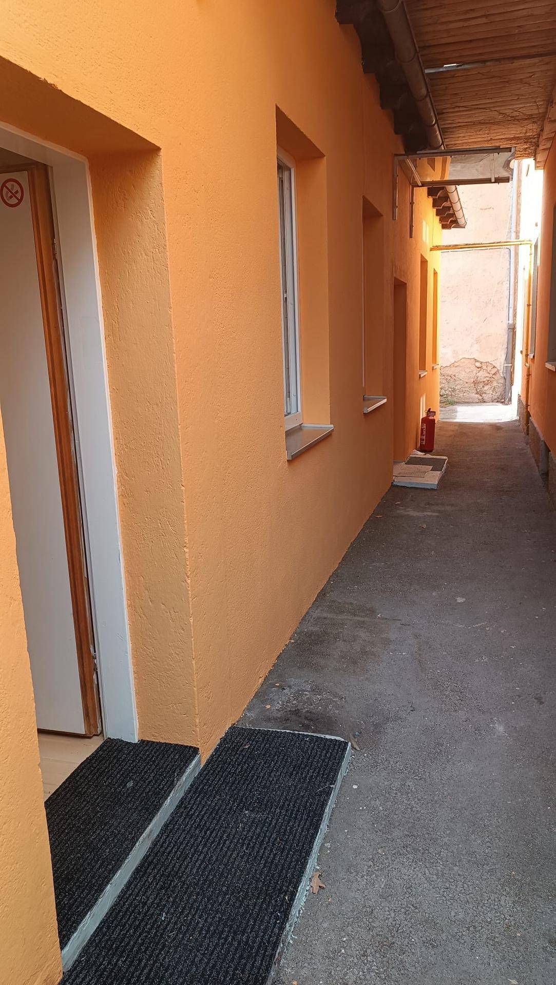 Enger Außenbereich zwischen zwei Gebäuden mit leuchtend orangefarbenen Wänden und einem Holzdach.