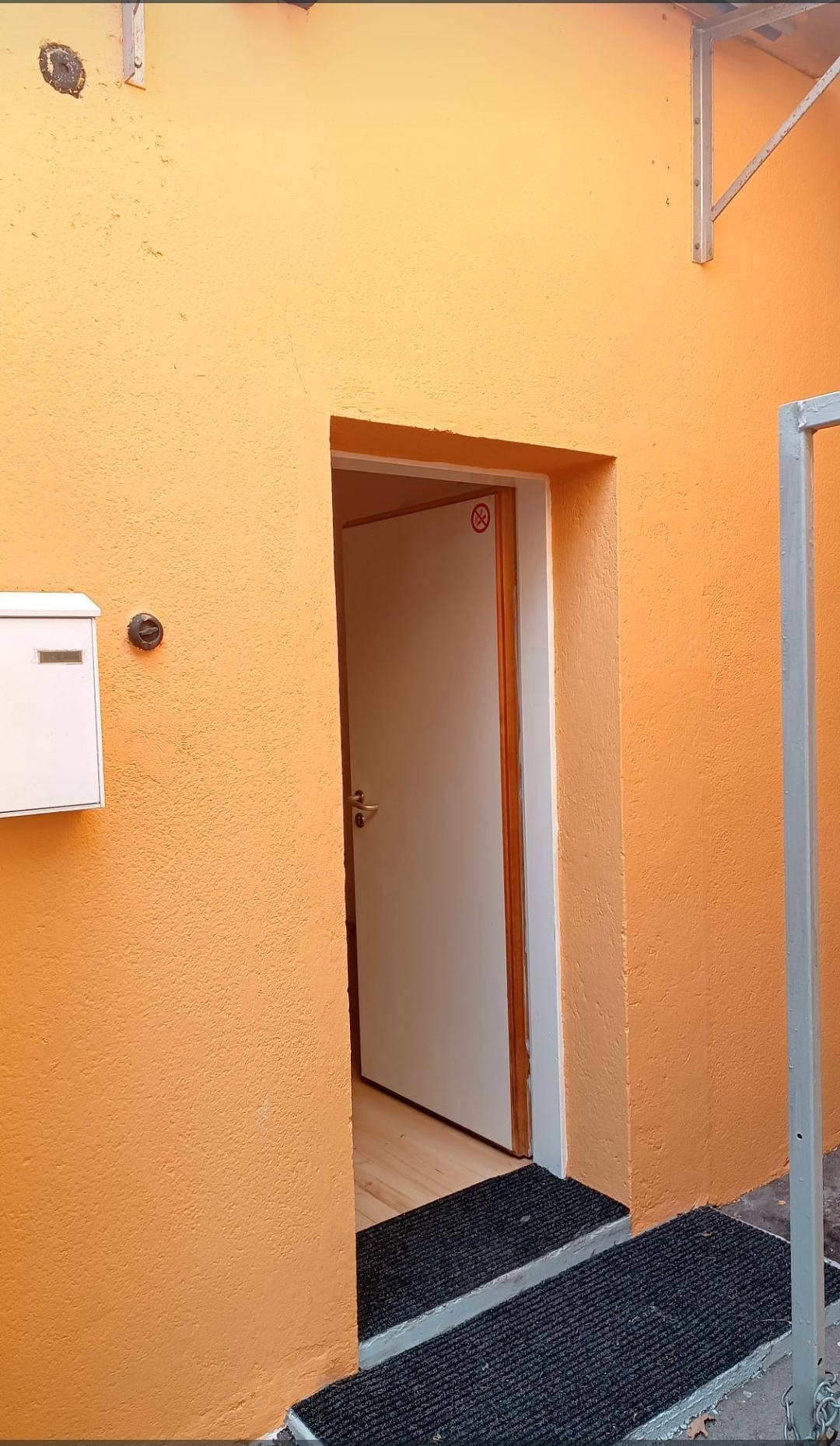 Eingangsbereich mit orangefarbener Fassade und einer weißen Tür, die in das Gebäude führt.