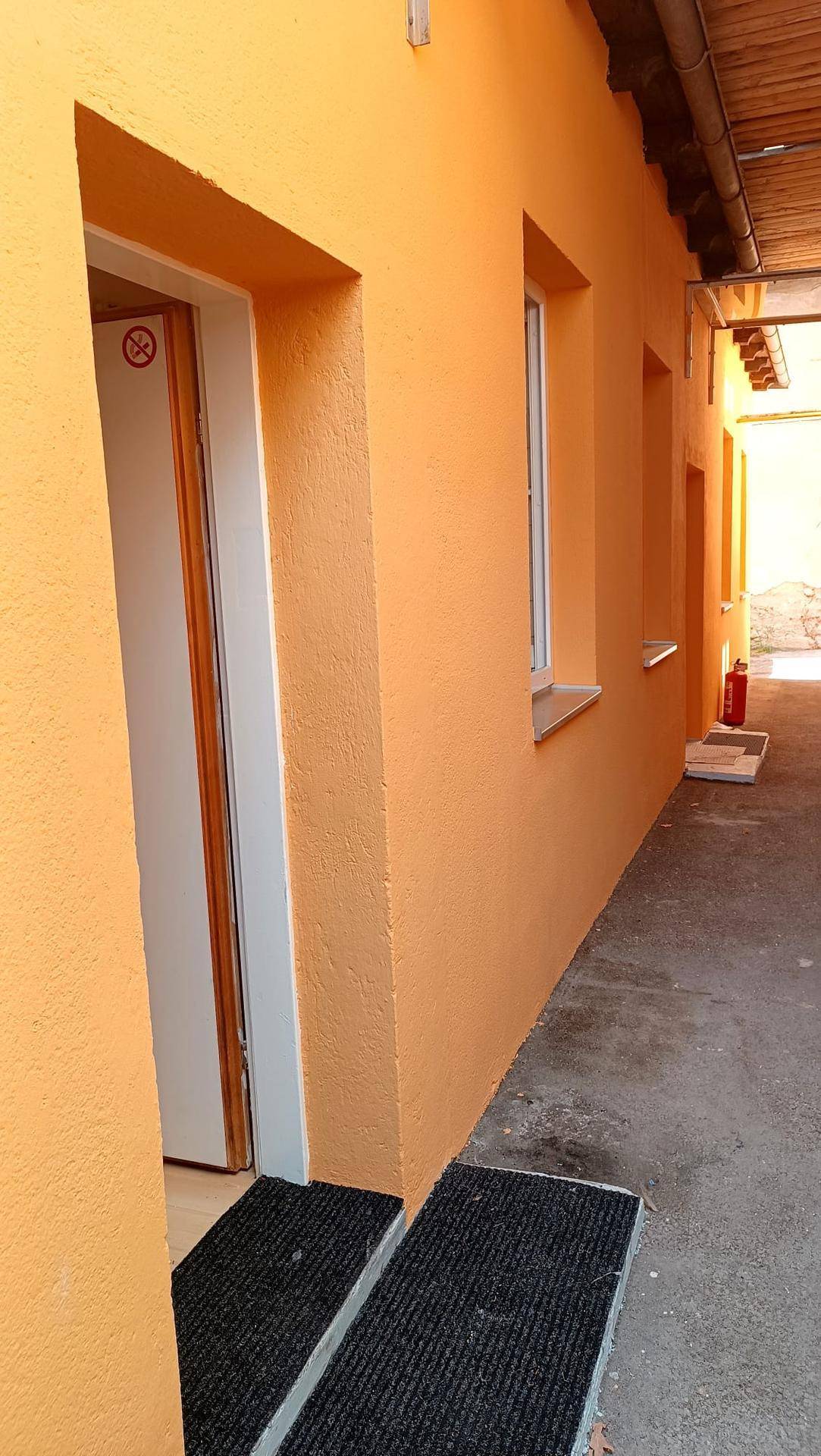 Außenansicht eines schmalen Ganges mit orangefarbenen Wänden und einem Eingangsbereich.