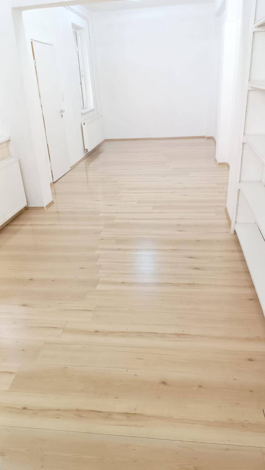 Geräumiger, heller Raum mit Holzboden und weißen Wänden, der einen aufgeräumten Eindruck macht.