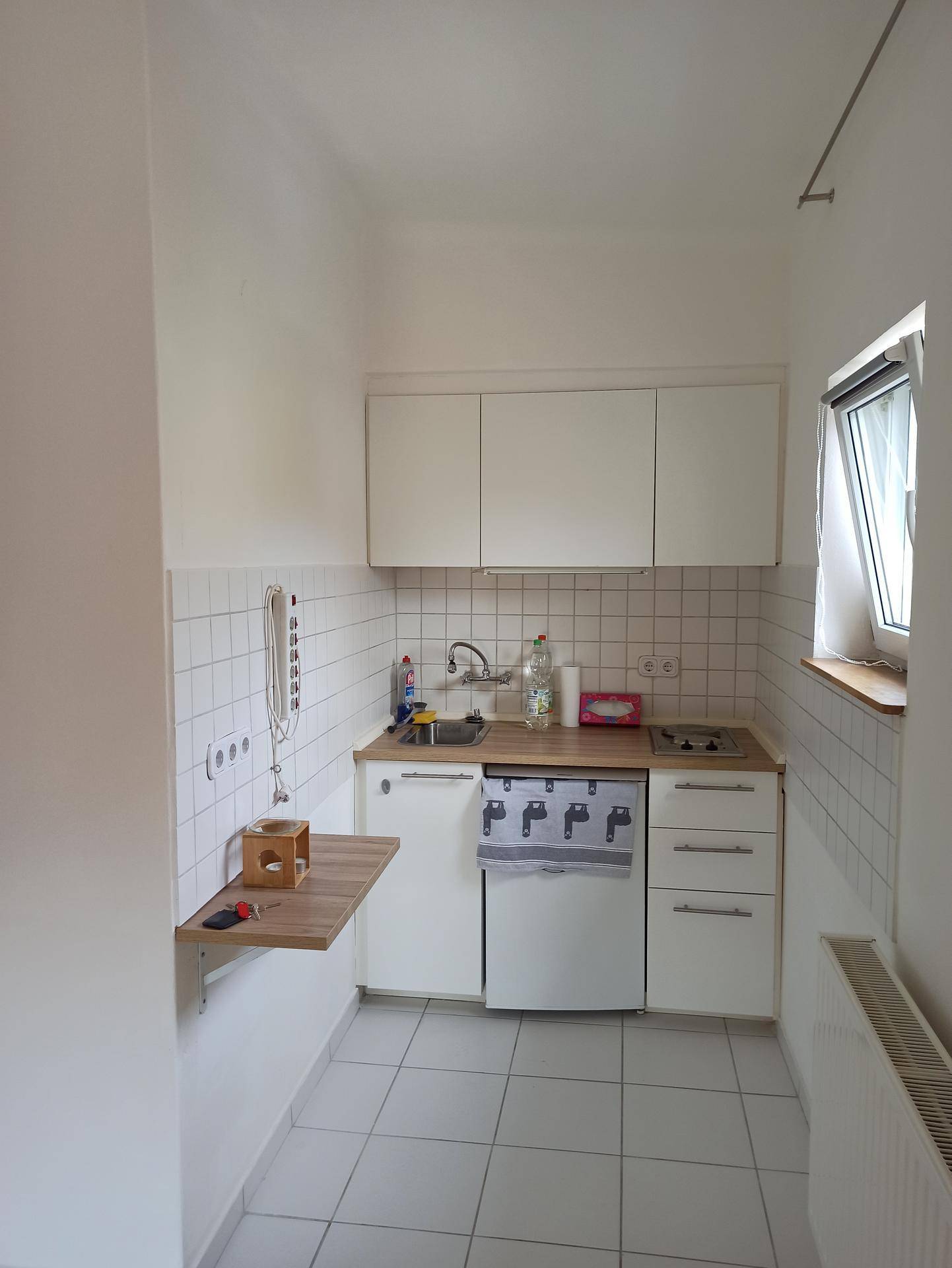 Kleine, funktionale Küchenzeile mit weißen Schränken, Fliesen und einem Fenster.