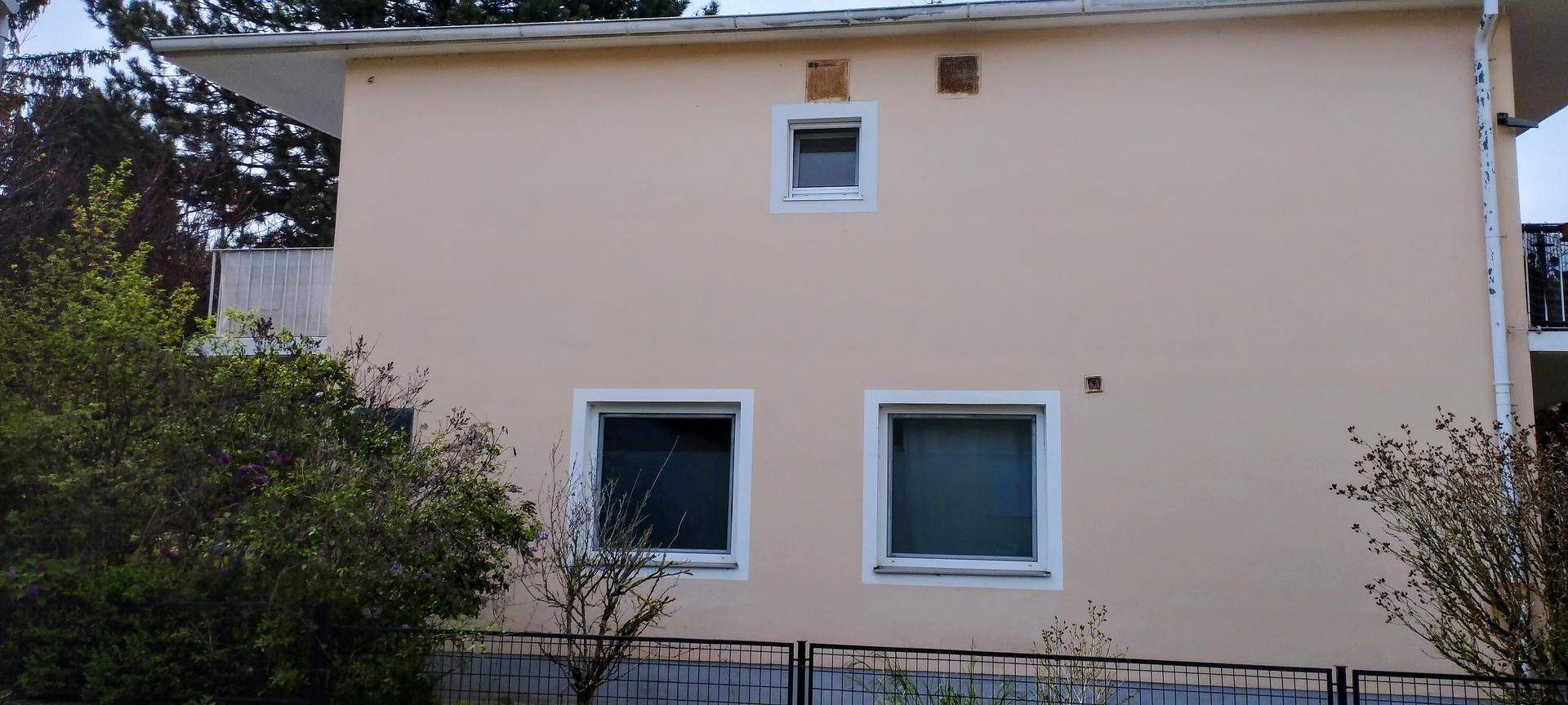 Seitenansicht der hellen Gebäudefassade mit mehreren Fenstern und einem Balkon.