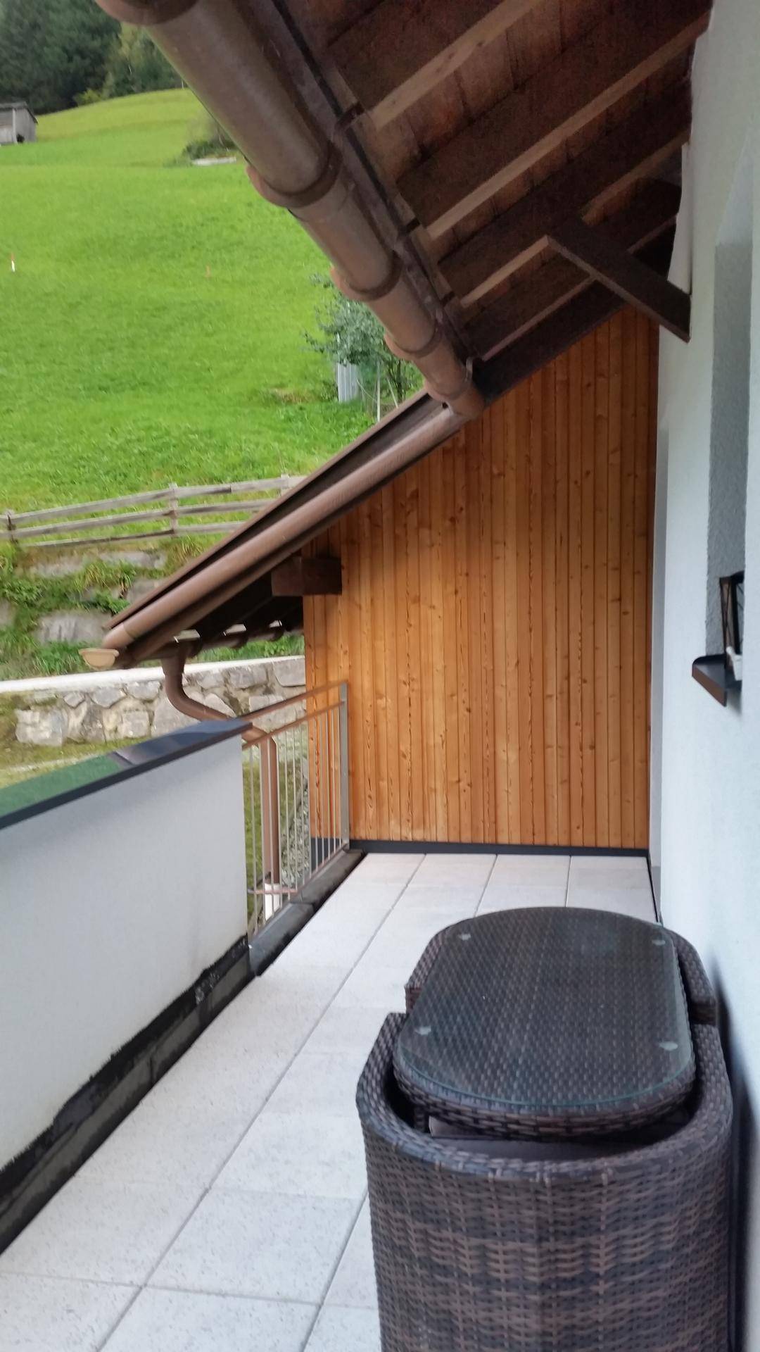 Schmaler Balkon mit Fliesenboden, Holzelementen und Blick ins Grüne.
