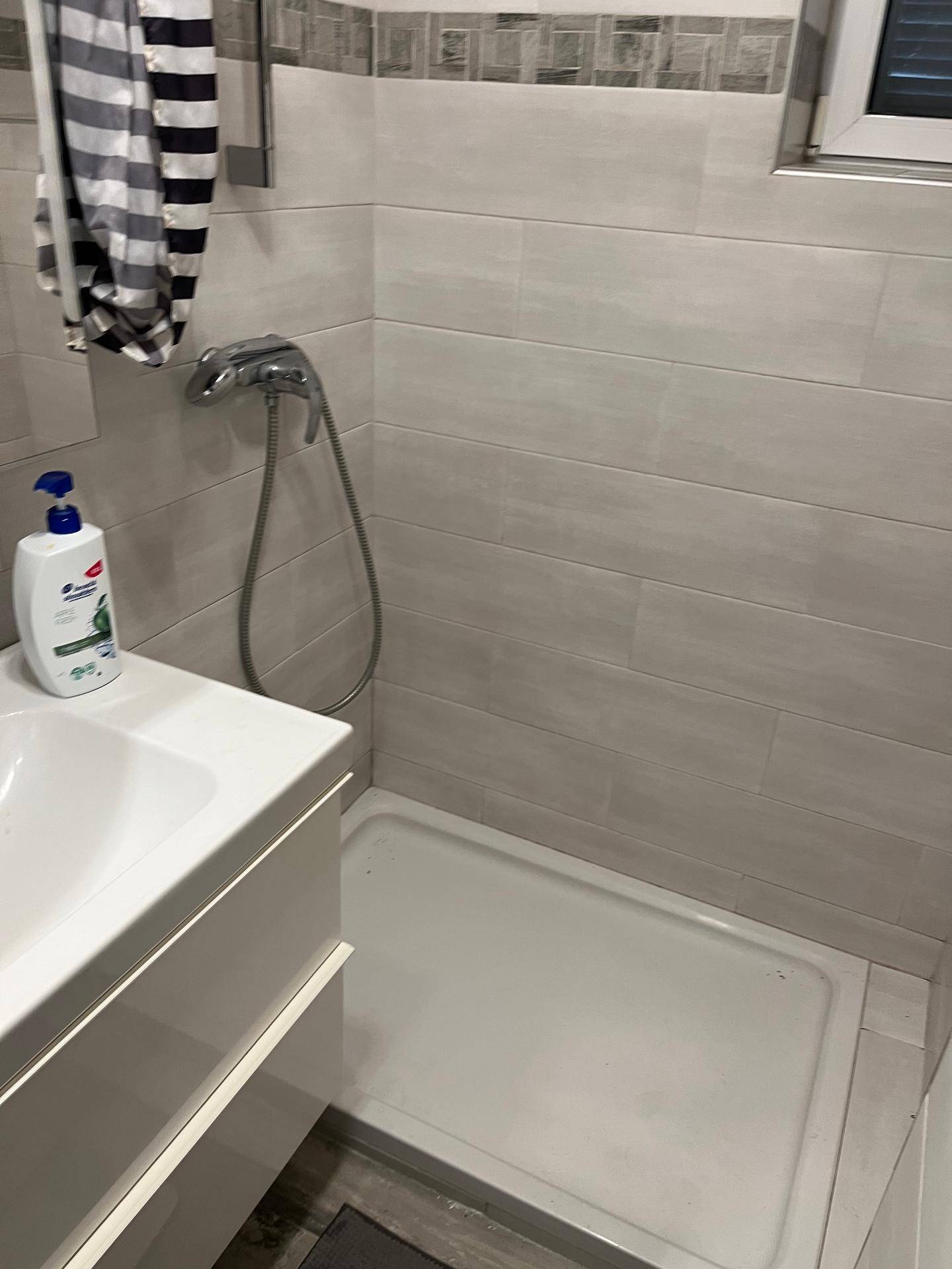 Modernes Badezimmer mit hellen Fliesen, Duschkabine und einem Waschbecken mit Unterschrank.
