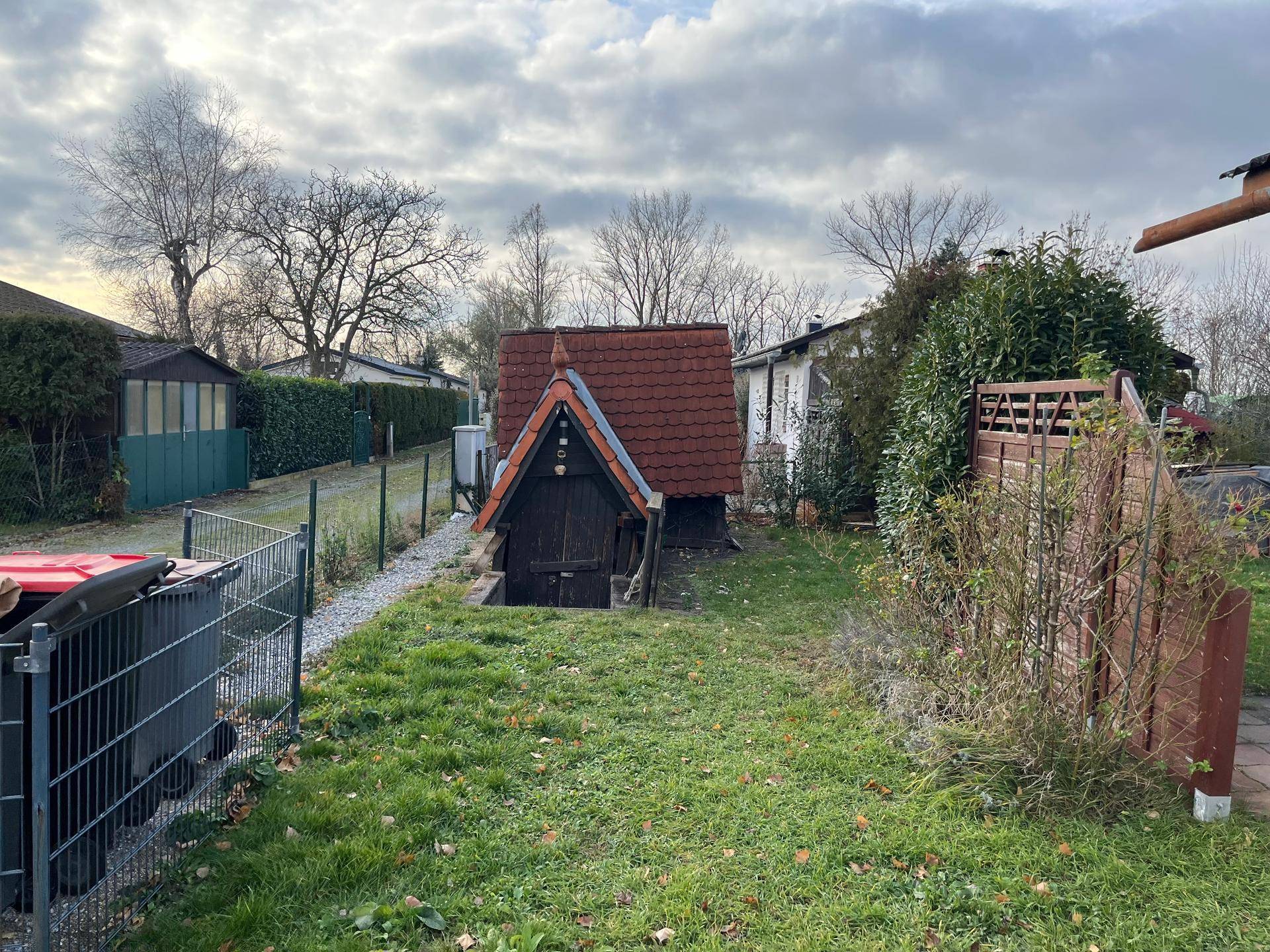 Gartenbereich mit Rasenfläche und einem kleinen, rustikalen Kellergebäude mit Ziegeldach.