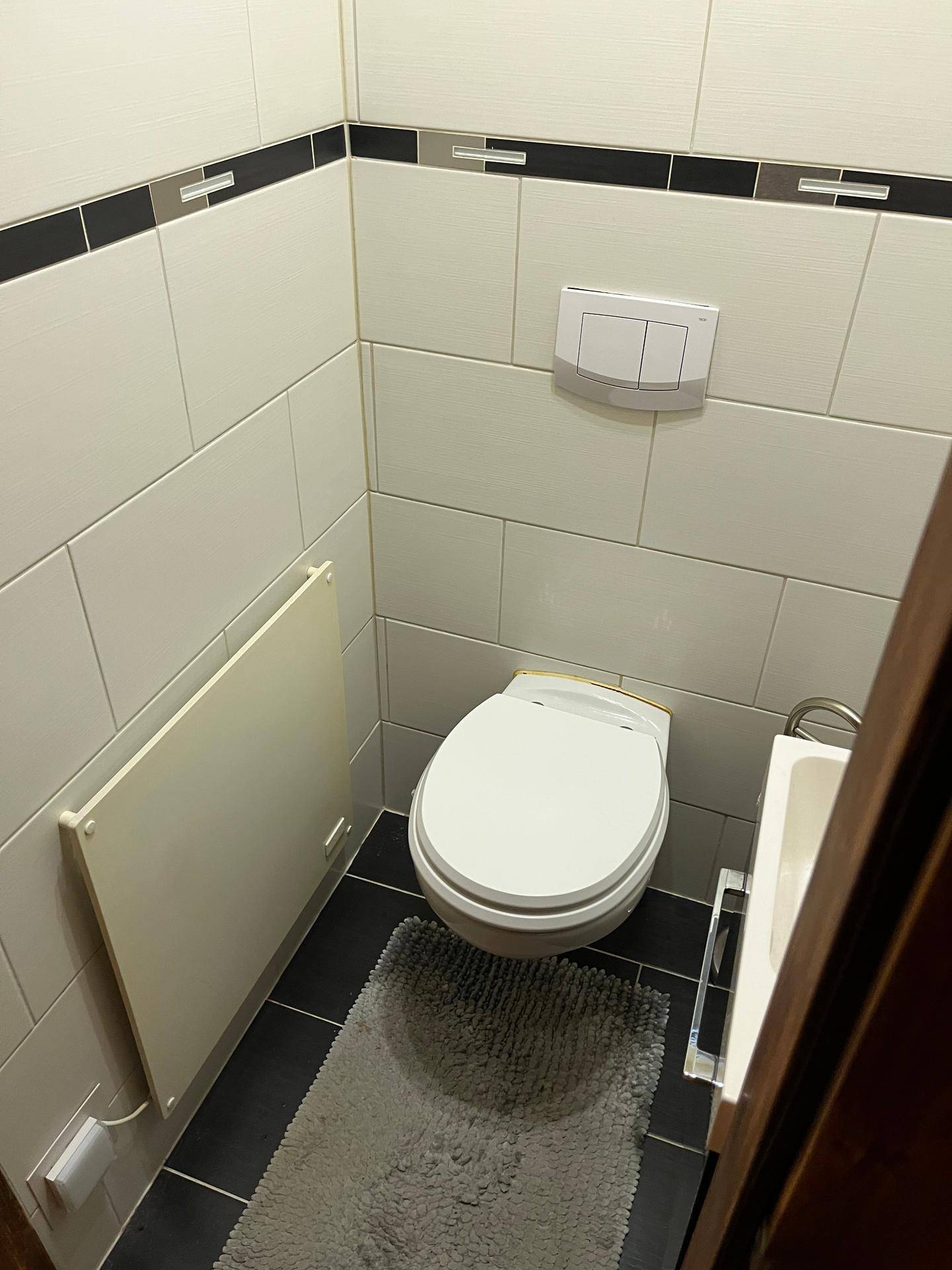 Separate Toilette mit Wand-WC, kleinem Waschbecken und modernen schwarz-weißen Fliesen.