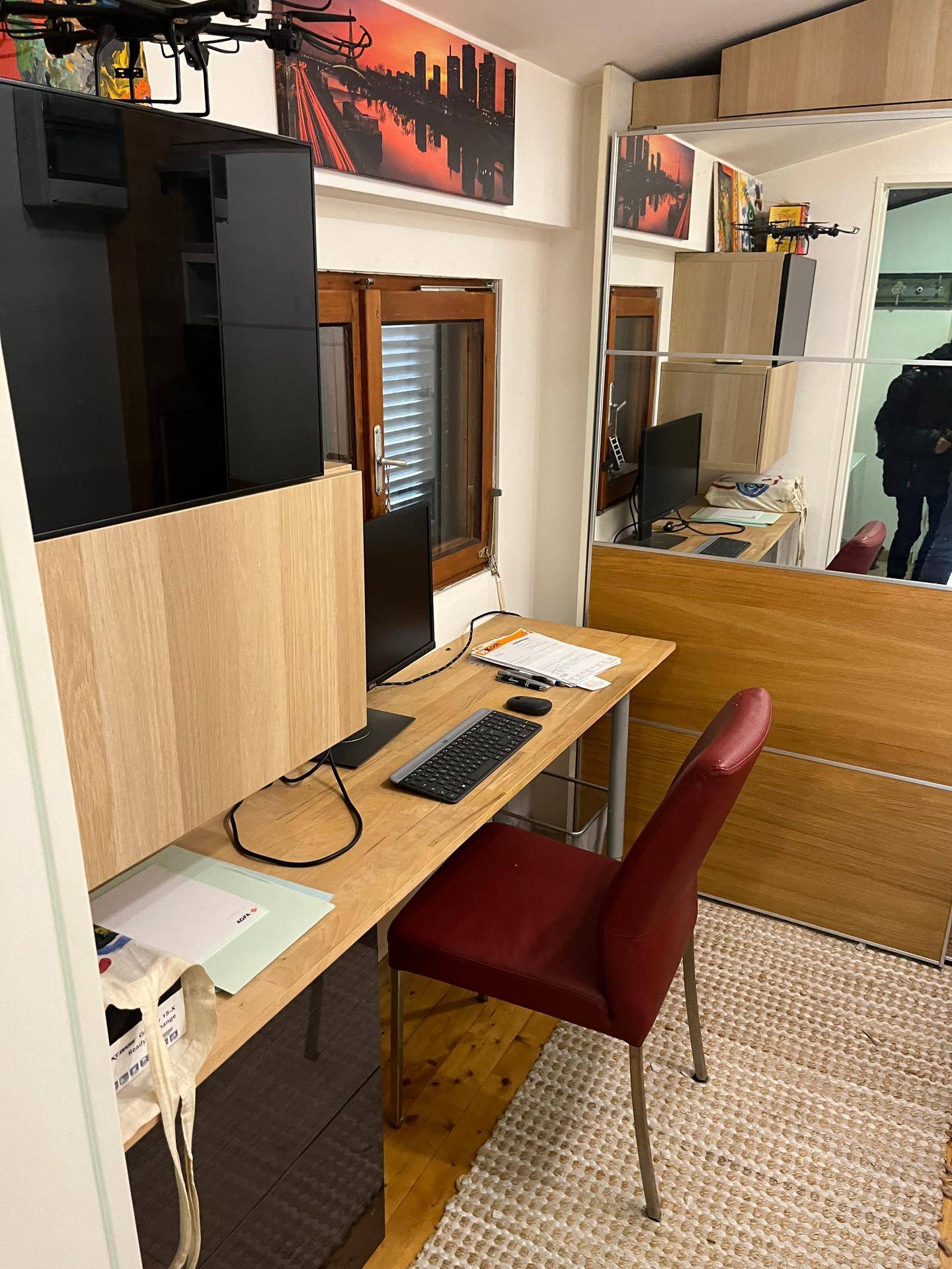 Kleiner Arbeitsbereich mit Holzschreibtisch, Computer und rotem Bürostuhl, ideal für Home-Office.