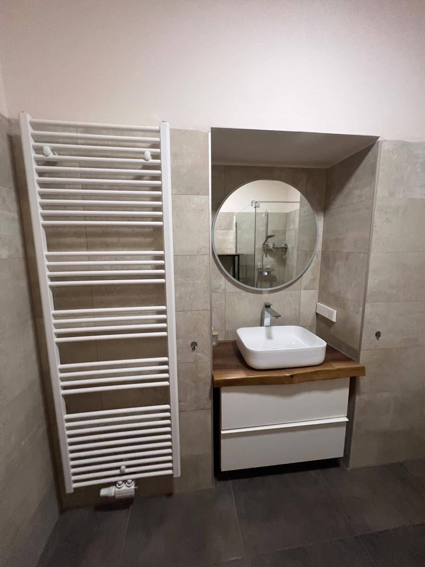 Modernes Badezimmer mit Heizkörper für Handtücher, Waschbecken und rundem Spiegel über dem Waschtisch.