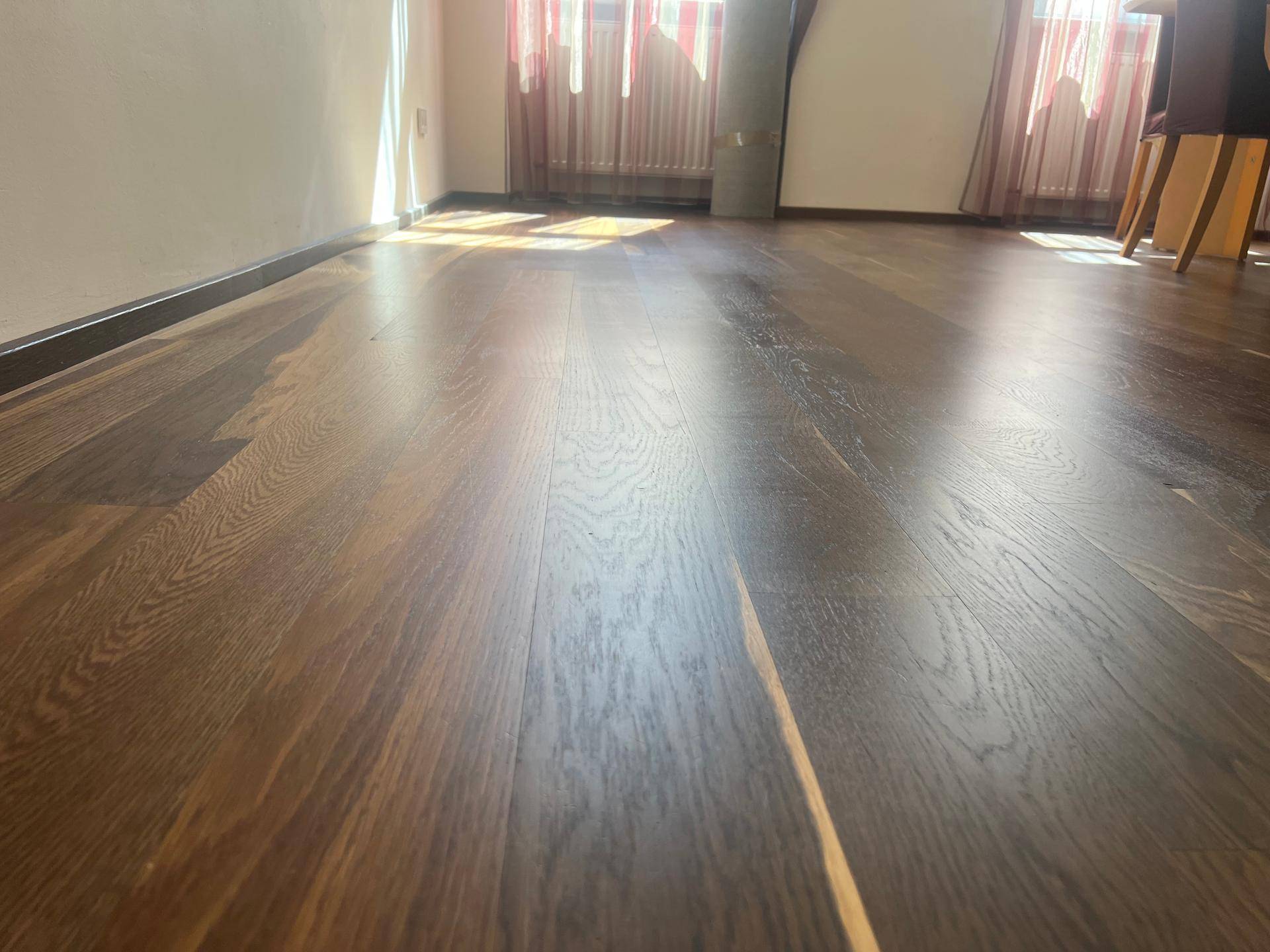 Nahaufnahme des dunklen Holzbodens, der das natürliche Licht reflektiert und eine warme Atmosphäre schafft.