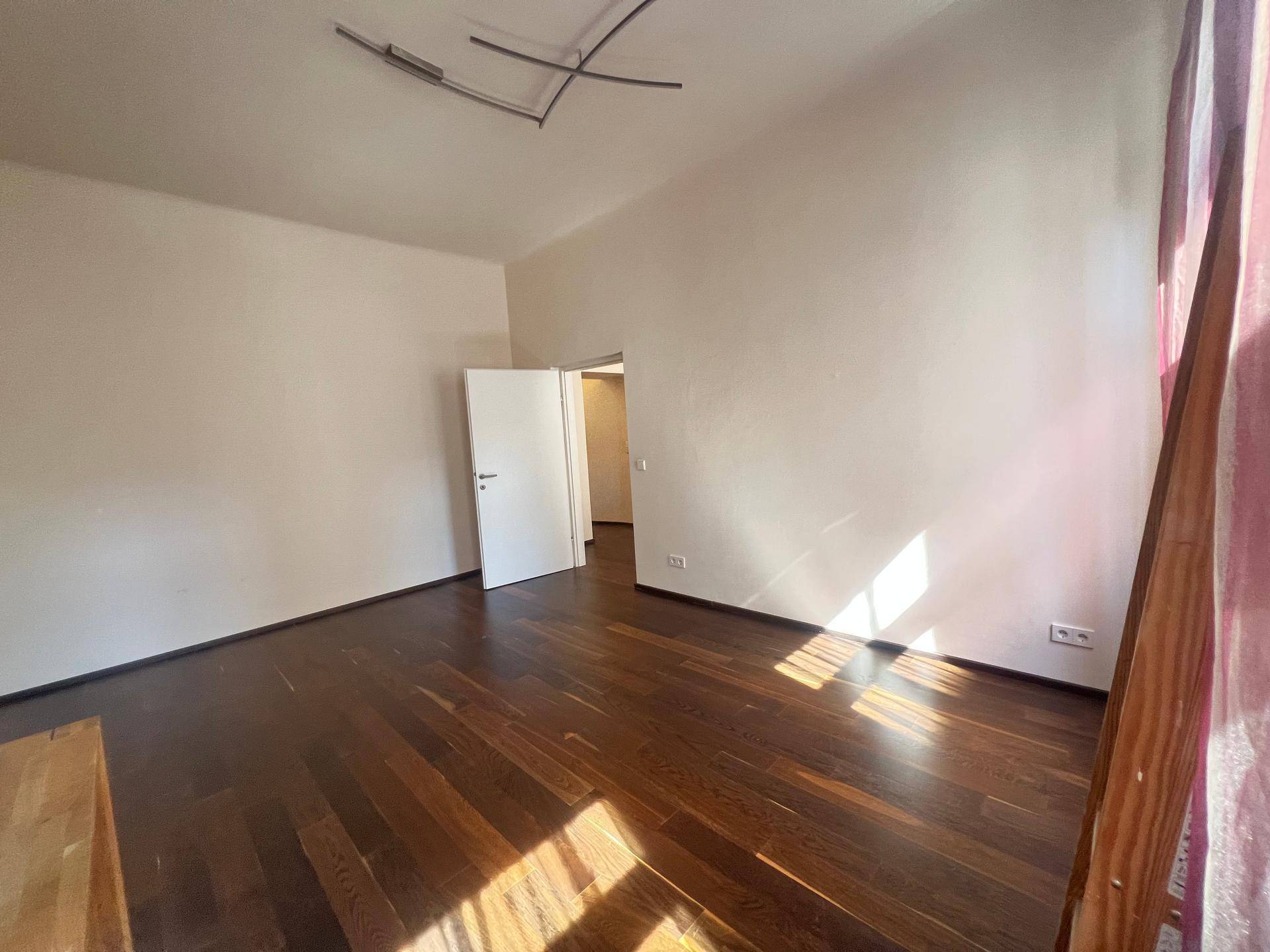 Geräumiger, heller Raum mit dunklem Holzboden und weiß gestrichenen Wänden, ideal für verschiedene Einrichtungsstile.