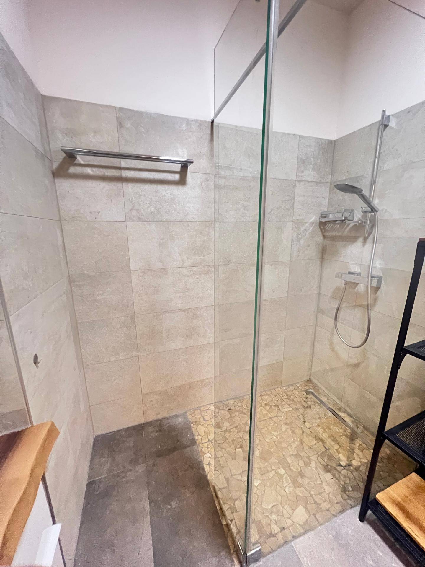 Begehbare Dusche mit Glaswand und Mosaikboden, umgeben von modernen, hellgrauen Fliesen.