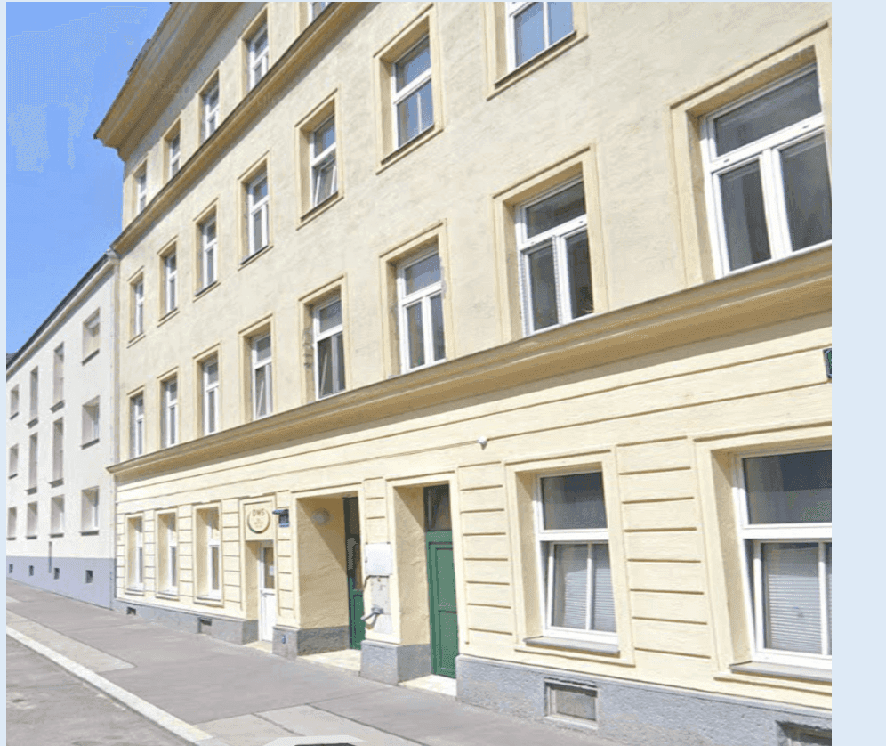 Klassische Fassade eines Altbaus mit vielen Fenstern und einem Eingangsbereich in hellem Gelbton.