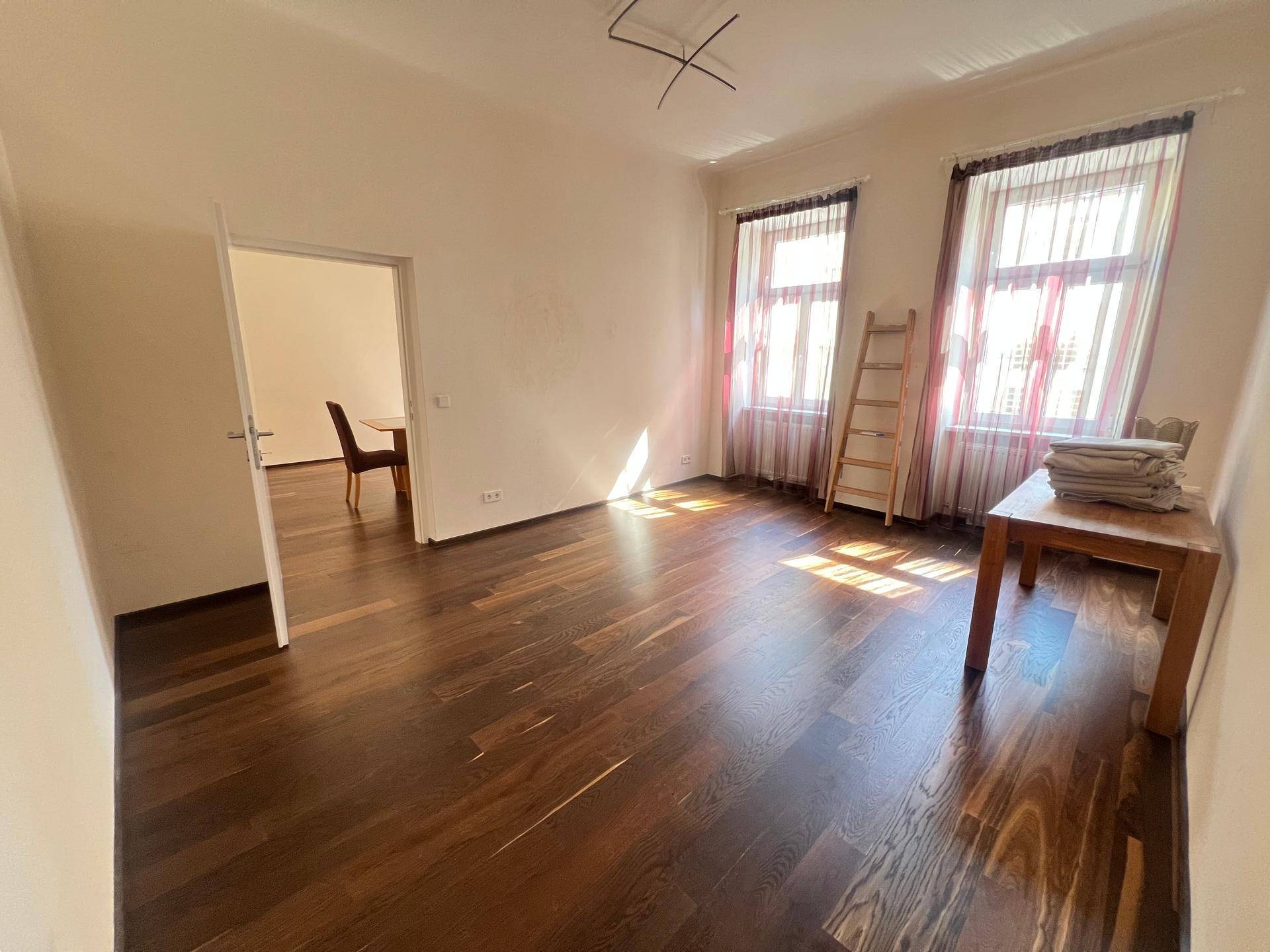 Heller Raum mit dunklem Holzboden und Fenstern, die viel Tageslicht hereinlassen, ideal für flexible Nutzung.