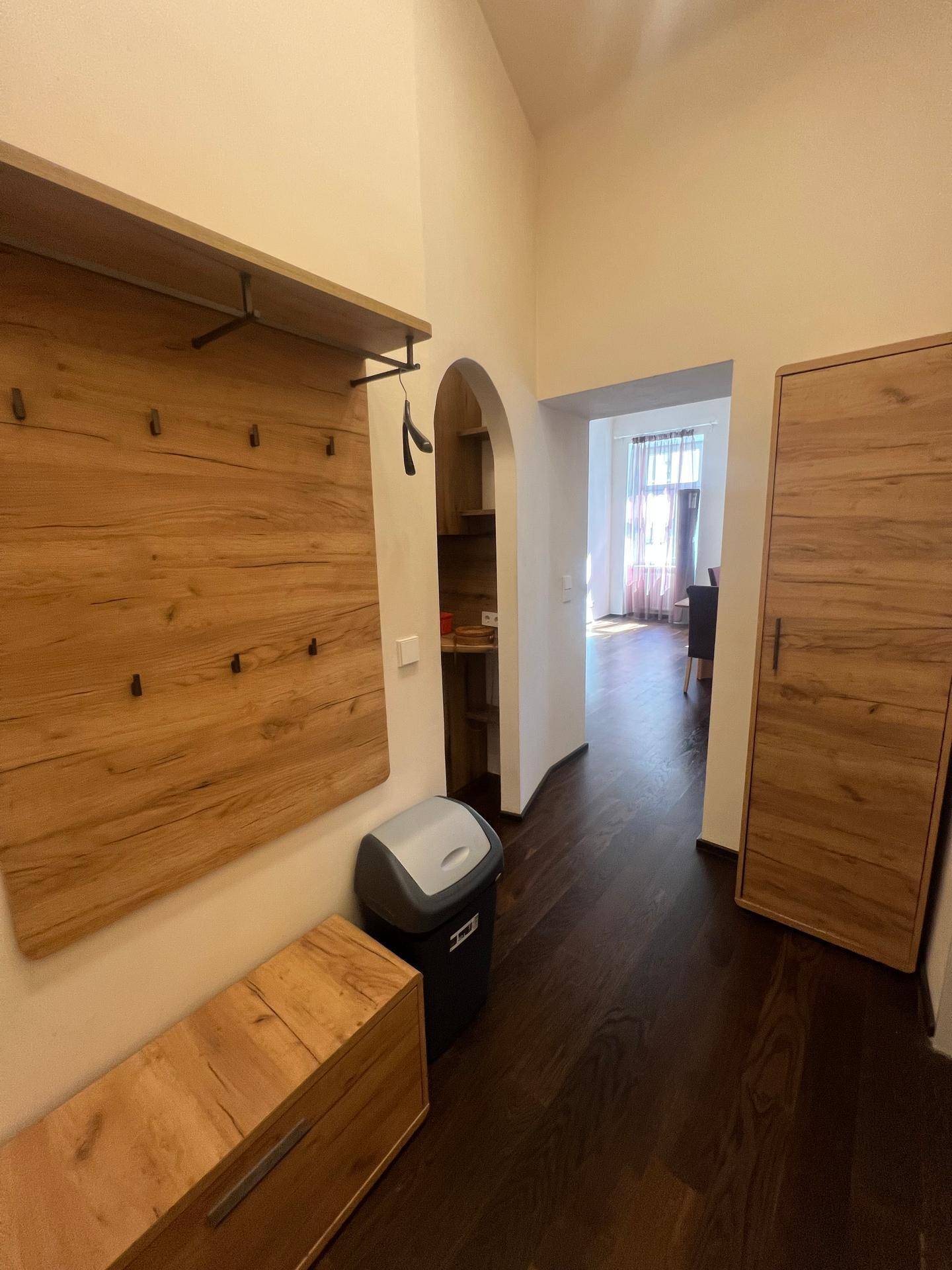 Eingangsbereich mit Garderobe aus Holz, dunklem Holzboden und einem Durchgang zur Küche.