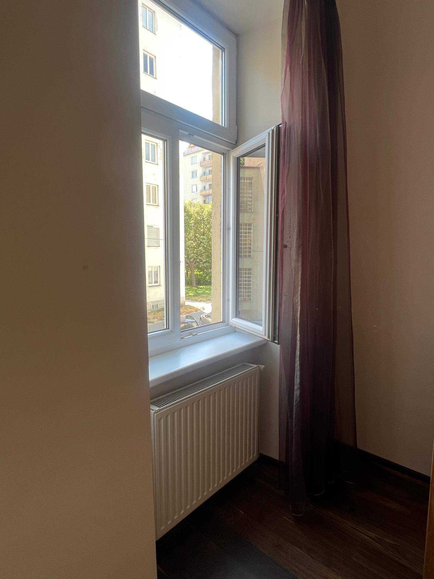Fenster mit Heizkörper darunter, das Tageslicht hereinlässt und einen Blick nach draußen ermöglicht.