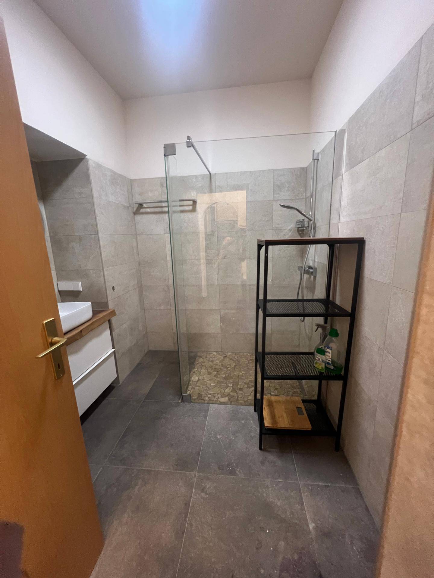 Geräumiges Badezimmer mit begehbarer Dusche, modernen Fliesen und einem praktischen Regal.