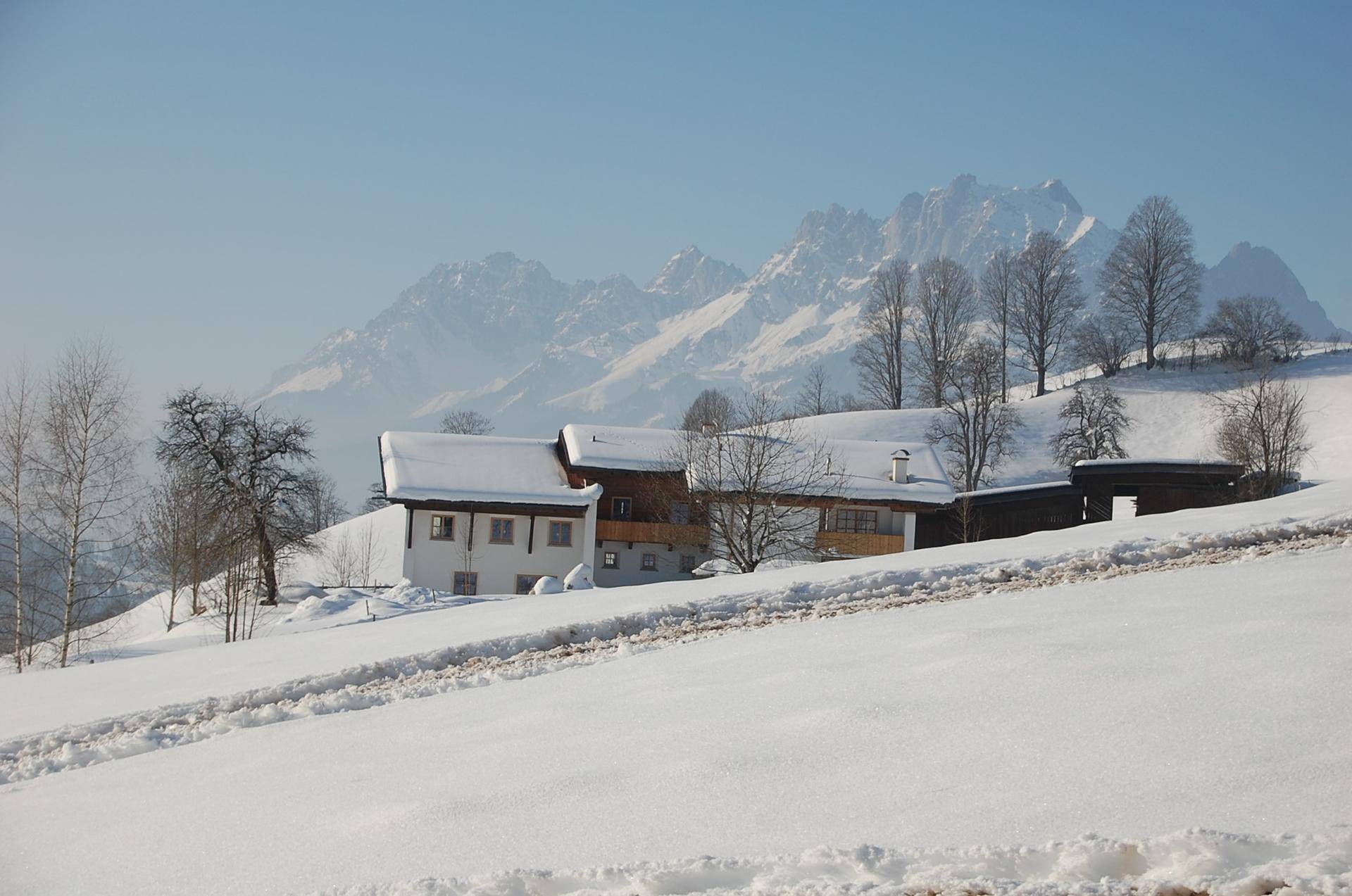 Verschneite Alpenlandschaft mit traditionellen Häusern und majestätischen Berggipfeln im Winter.