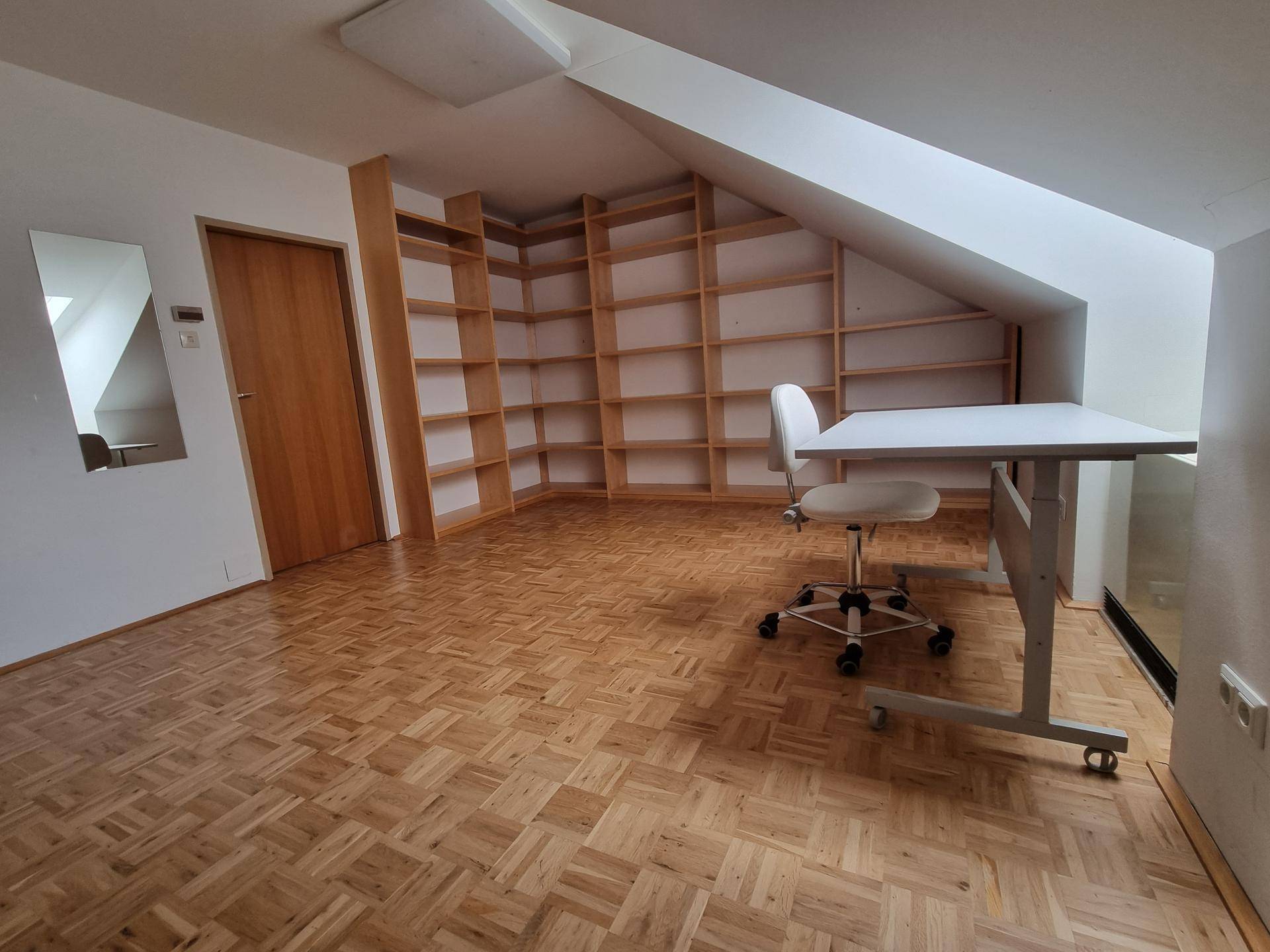 Dachgeschoss-Büro mit Parkettboden, integrierten Regalen und Schreibtisch unter der Dachschräge.