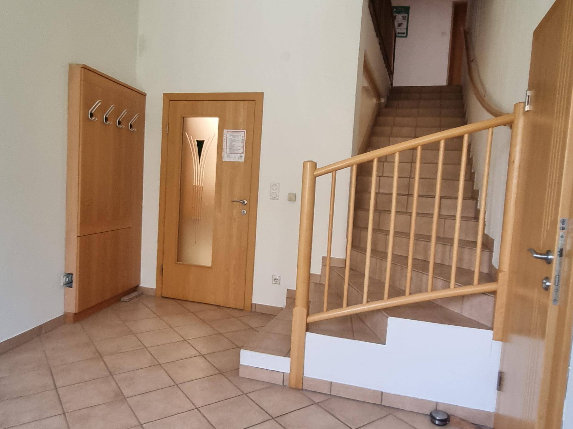 Eingangsbereich mit gefliestem Boden, Garderobe und Holztreppe zum Obergeschoss.