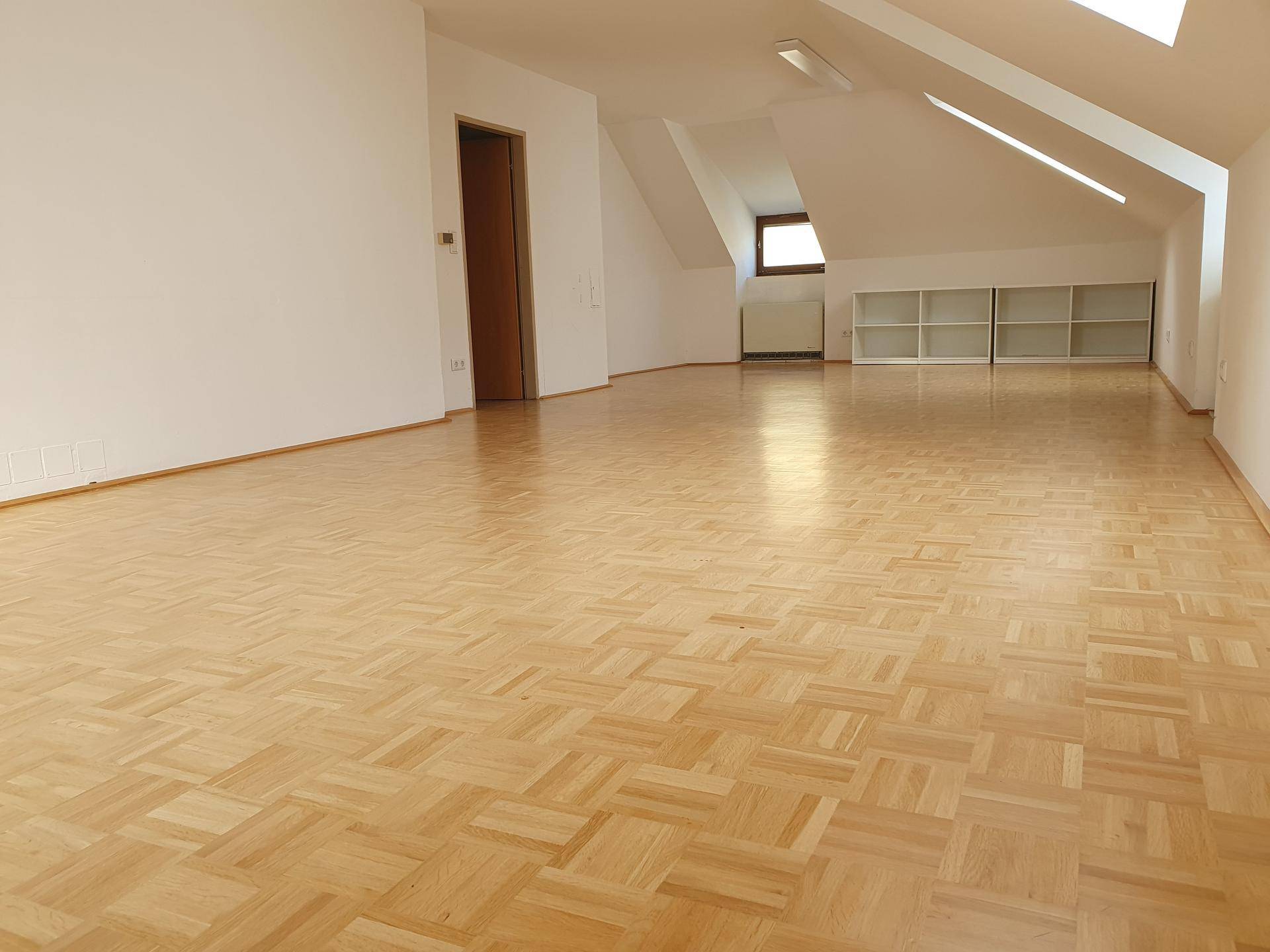 Helles Dachgeschoss mit Parkettboden und praktischen Einbauregalen entlang der Wand.