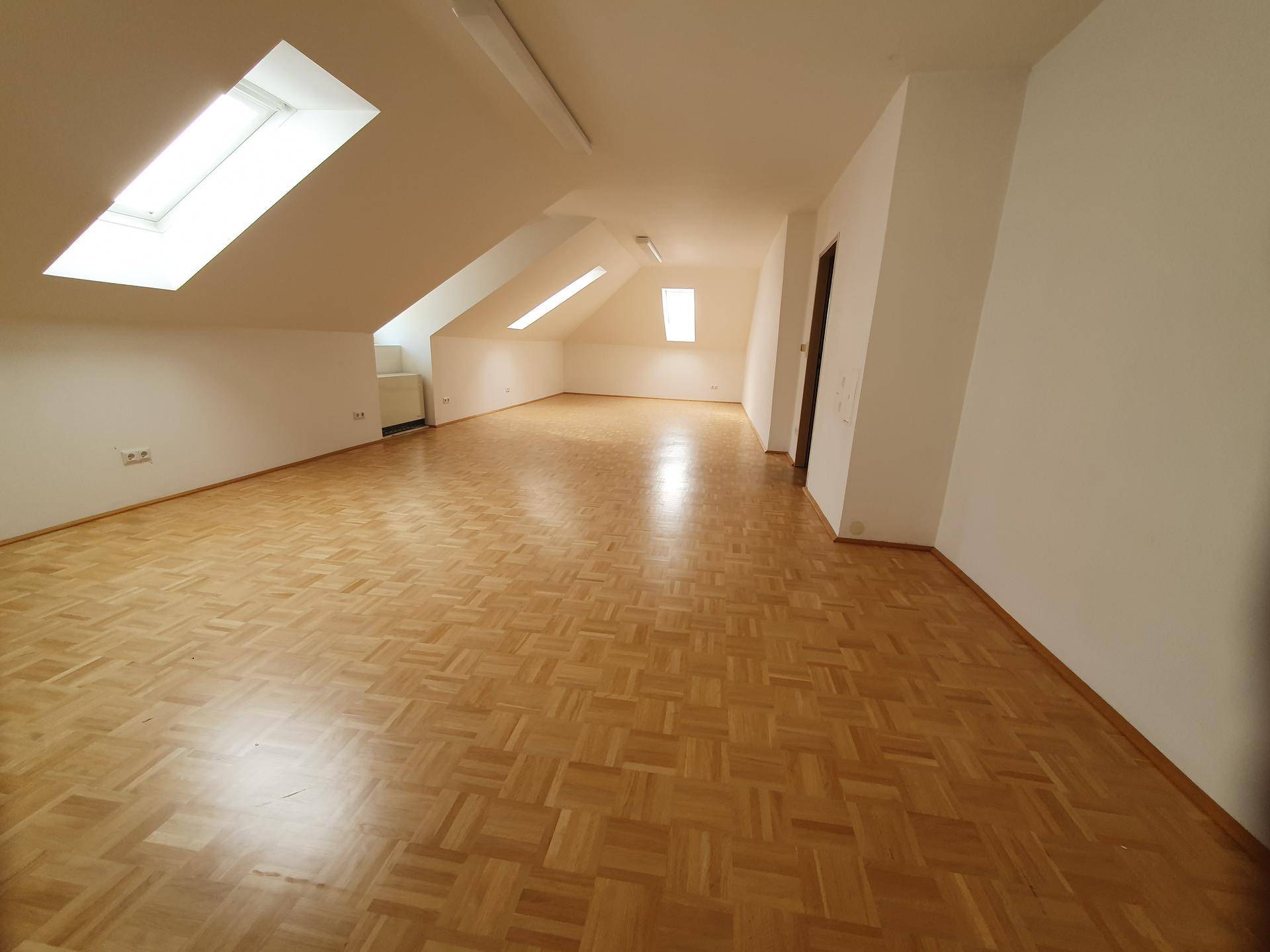 Geräumiger Dachbodenraum mit Parkettboden und mehreren Dachfenstern für Helligkeit.