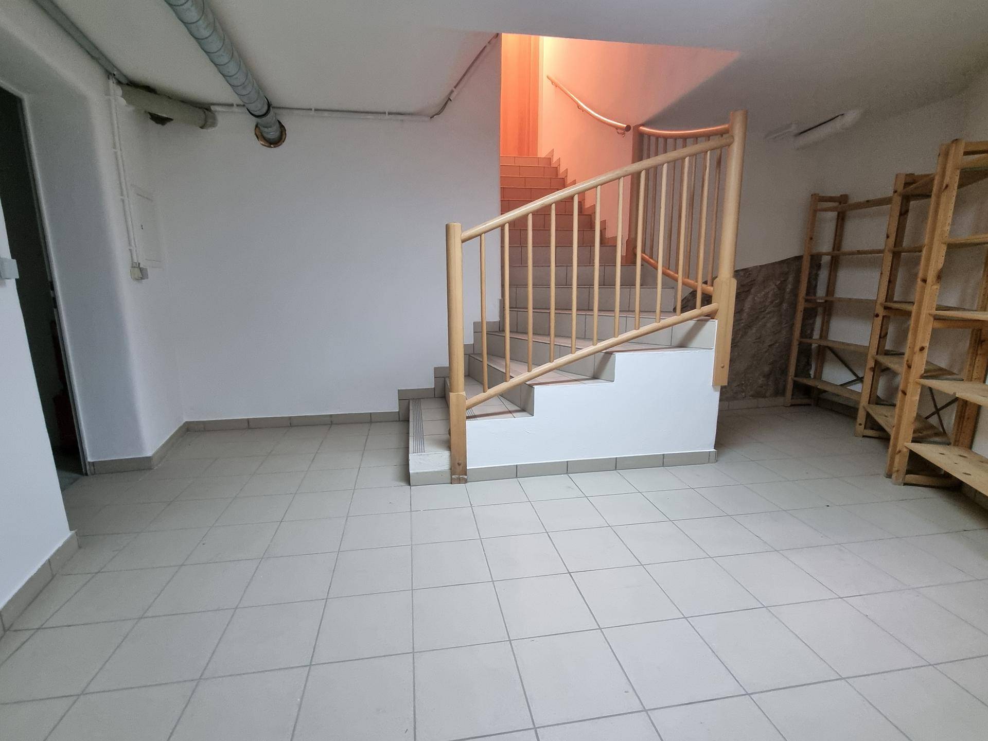 Kellerraum mit gefliestem Boden, Holztreppe und Regalen für zusätzlichen Stauraum.