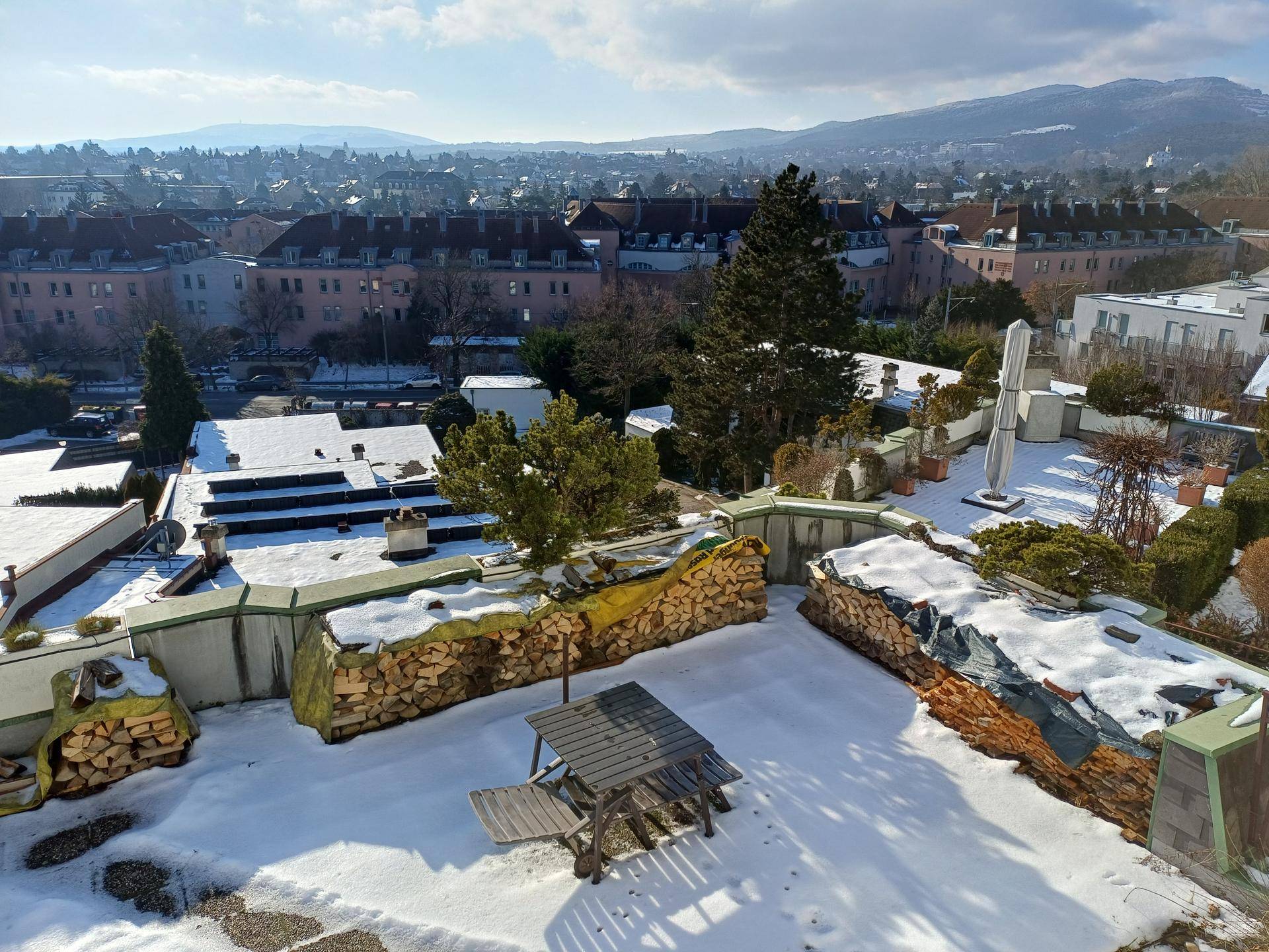 Dachterrasse im Winter mit Schnee bedeckt, Sitzgelegenheiten und Blick auf die verschneite Stadt.
