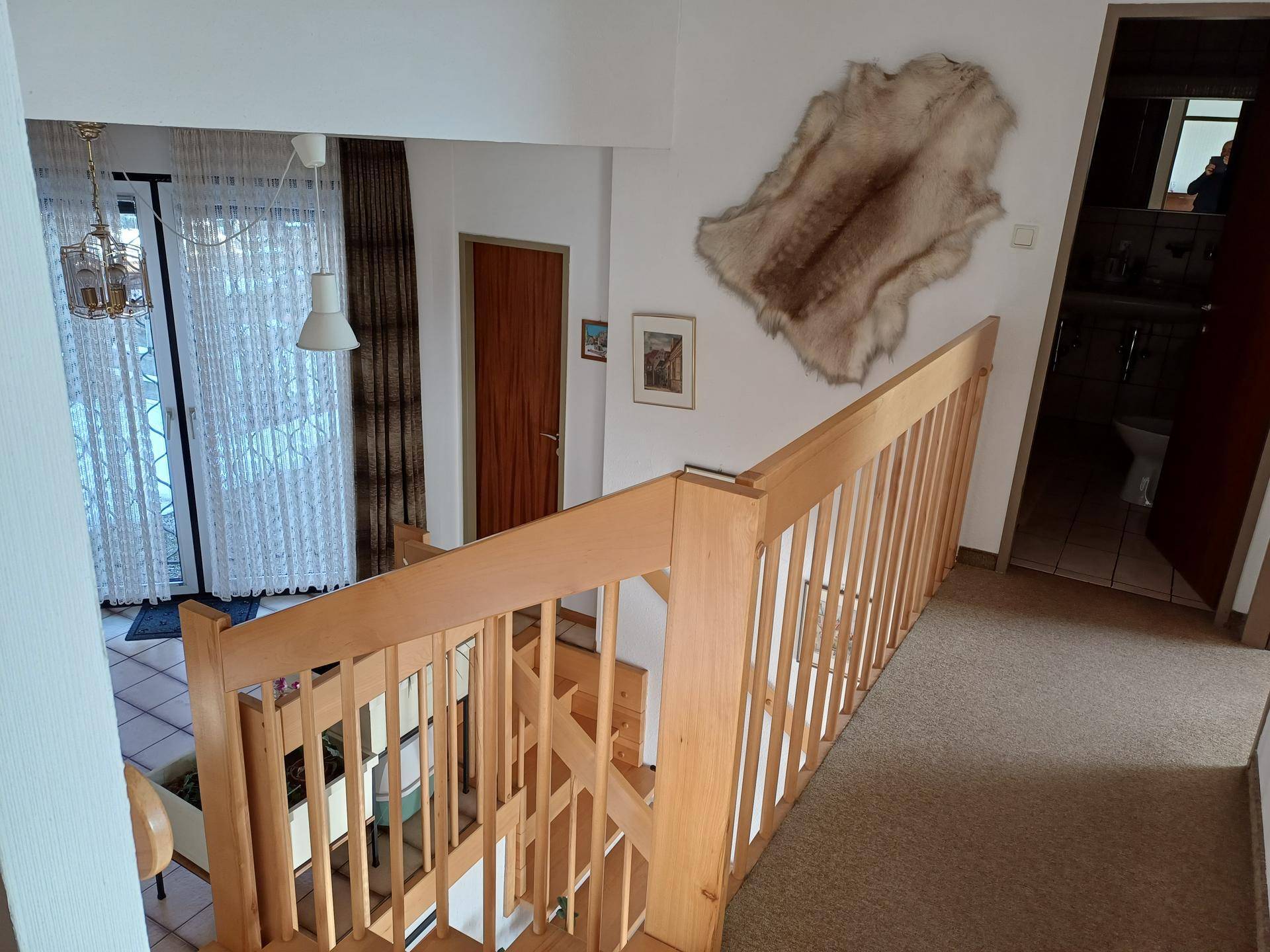Flur mit Holztreppe und einem dekorativen Fell an der Wand, führt zu weiteren Räumen.