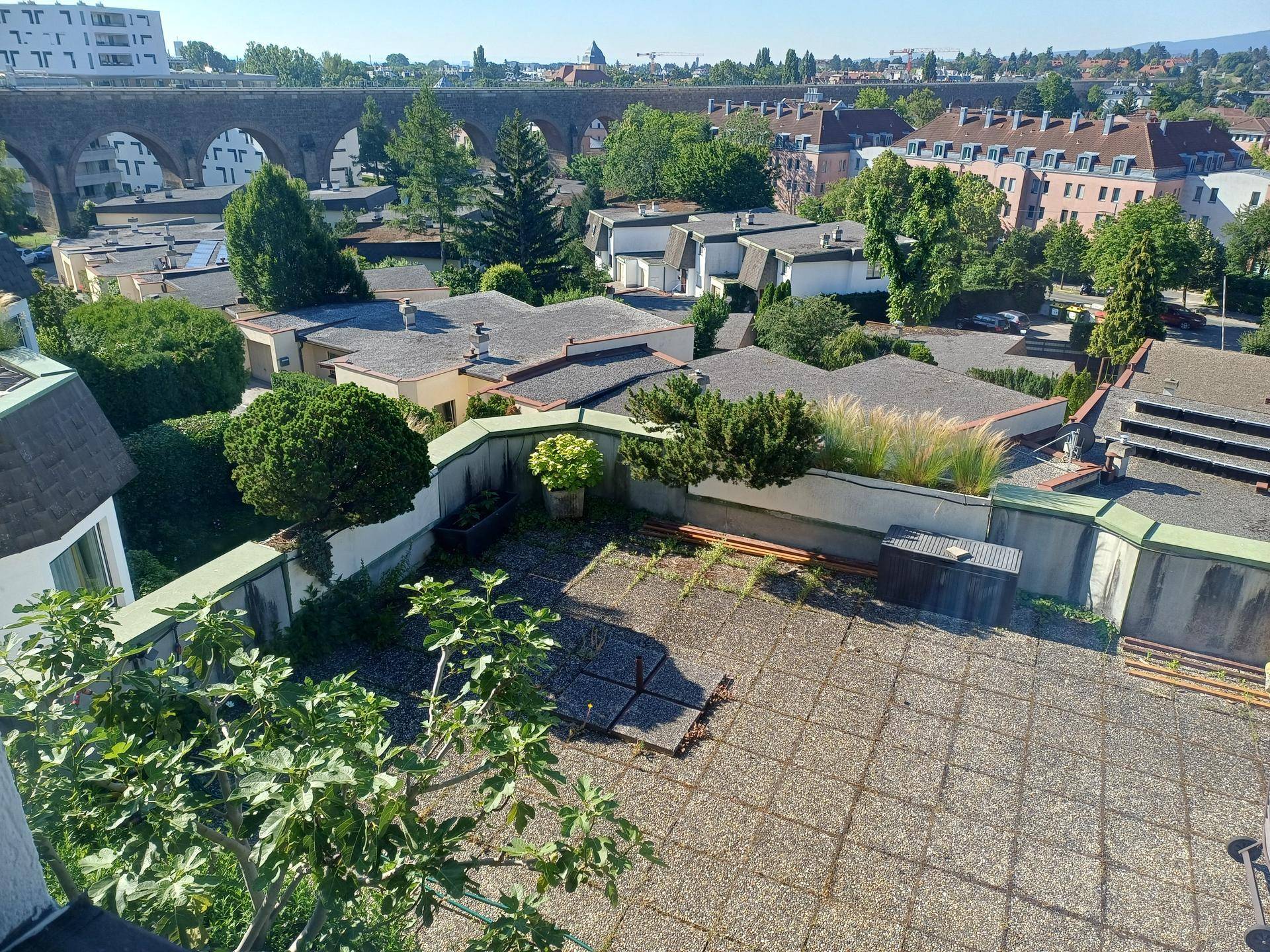 Dachterrasse mit Blick auf die Stadt und ein historisches Viadukt unter blauem Himmel.