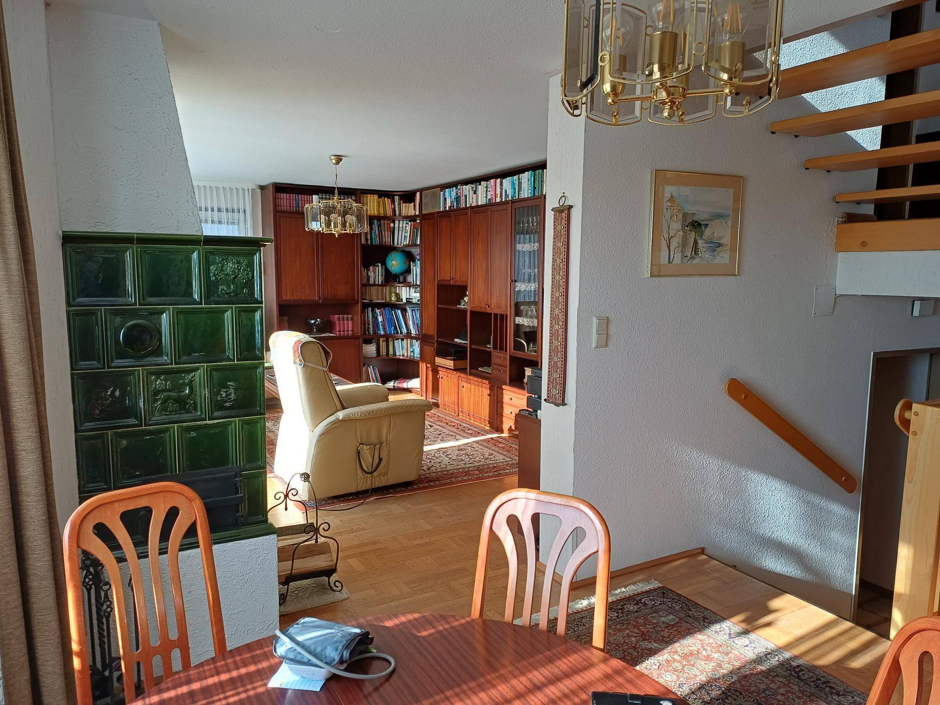 Gemütlicher Wohn-Essbereich mit traditionellem Kachelofen, Holzmöbeln und offener Treppe.