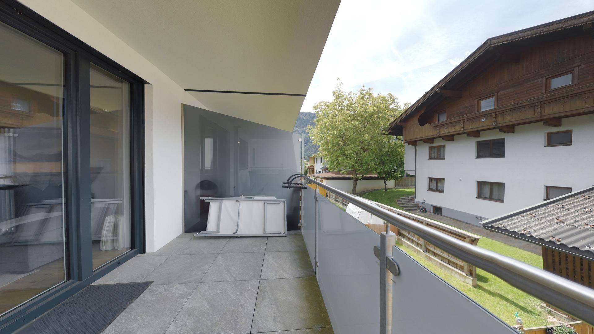 Geräumiger Balkon mit Fliesenboden und Blick auf die grüne Umgebung und Berge.