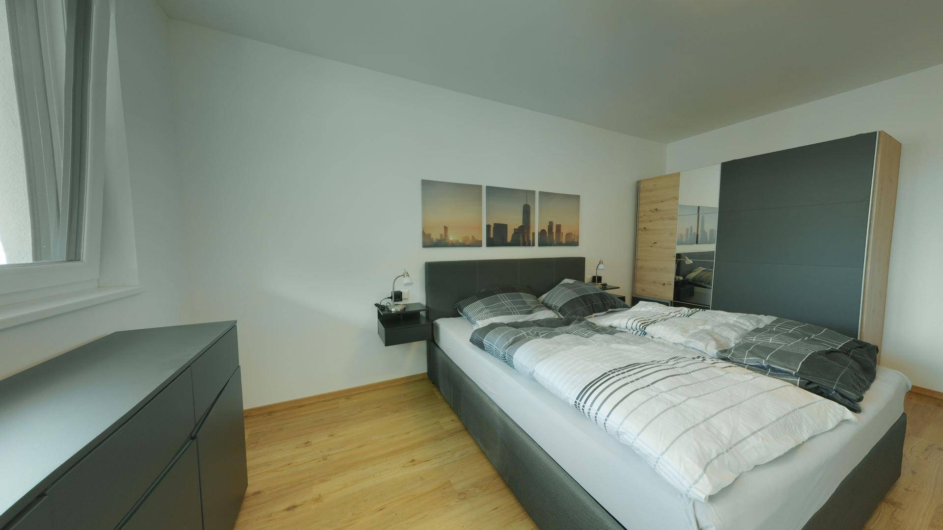 Modernes Schlafzimmer mit Doppelbett, Holzboden und dunklen Möbeln.