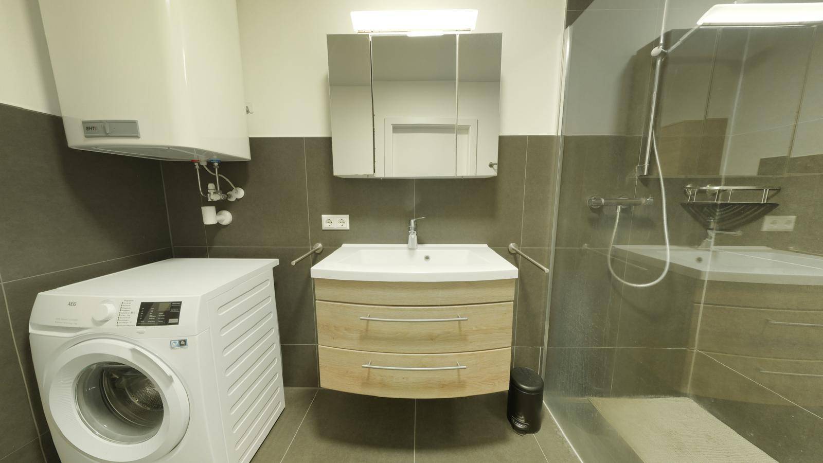 Modernes Badezimmer mit Dusche, Waschmaschine und Waschbeckenunterschrank.