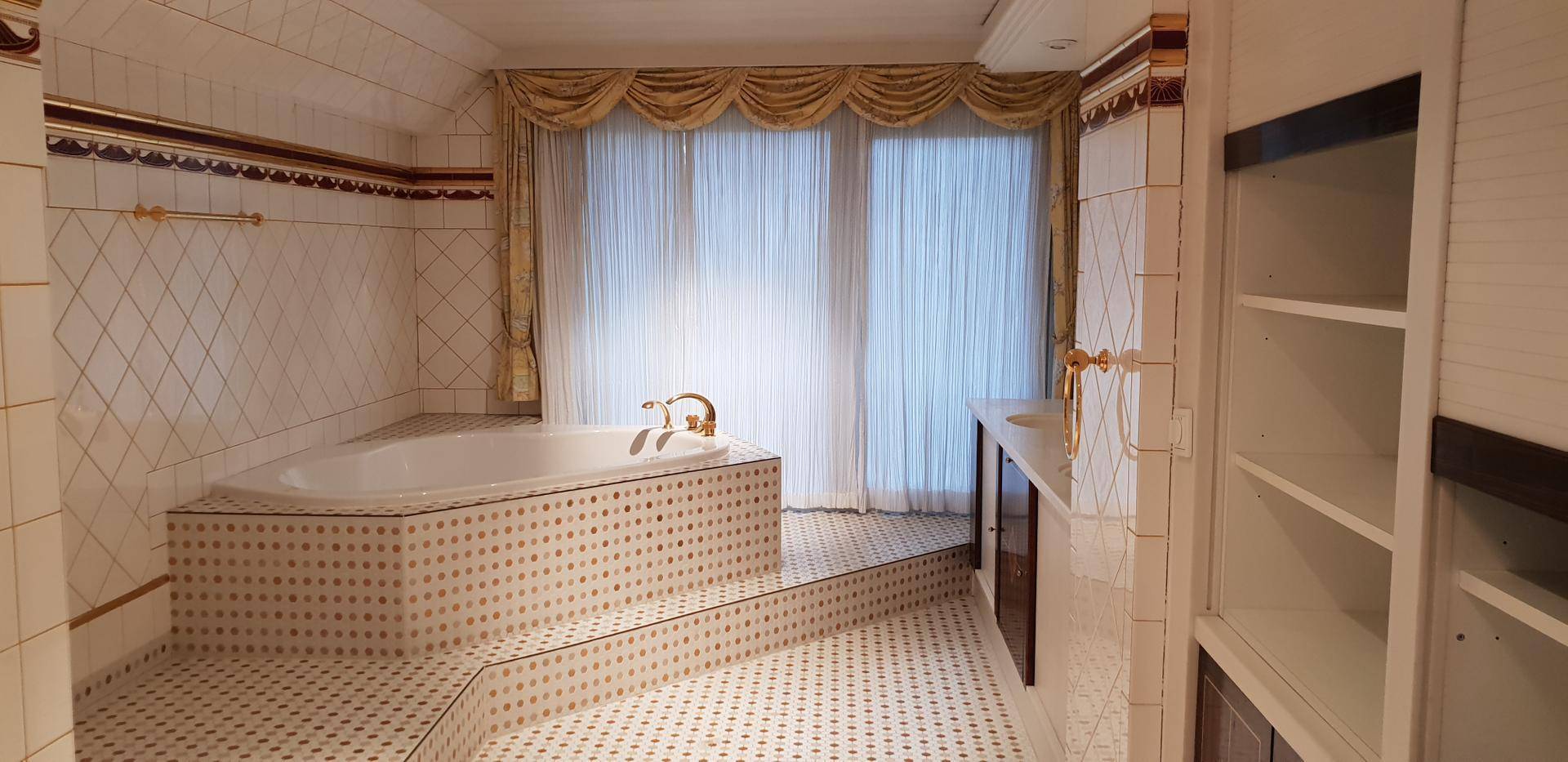 Geräumiges Badezimmer mit Eckbadewanne, doppelten Vorhängen und gemusterten Fliesen.