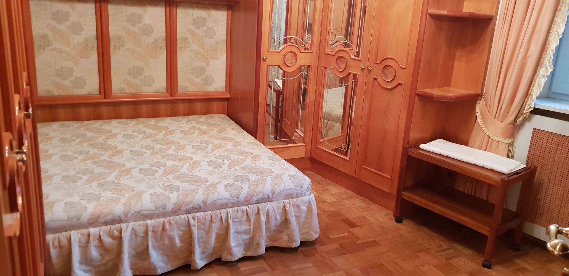 Schlafzimmer mit Holzeinbauschränken, Parkettboden und floral gemustertem Bett.