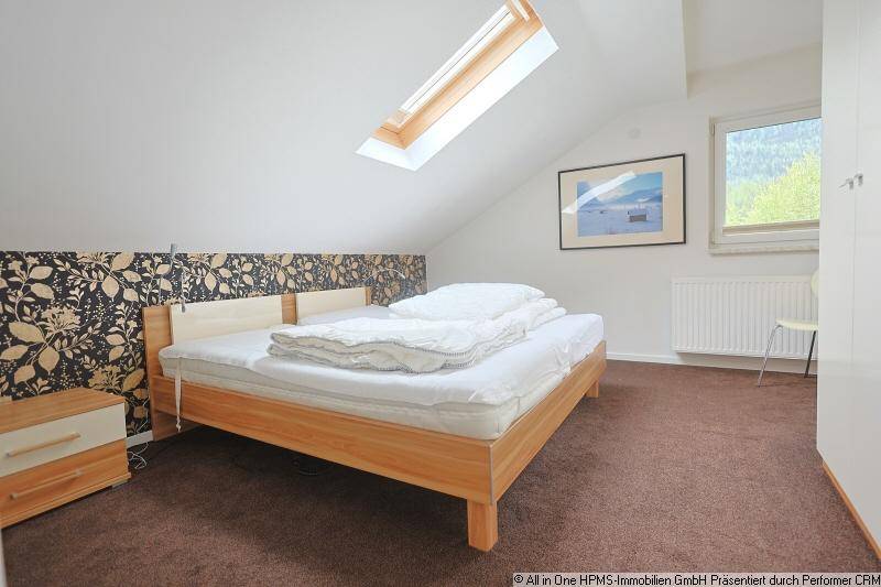 Helles Schlafzimmer im Dachgeschoss mit Dachfenster, Teppichboden und Bergblick.