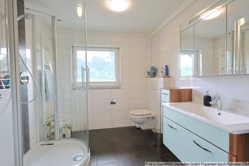Modernes Badezimmer mit Duschkabine, Fenster, Waschtisch und Spiegelschrank.