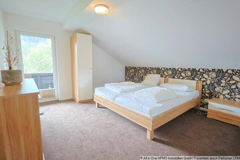 Schlafzimmer im Dachgeschoss mit schräger Decke, gemusterter Tapete und Balkonzugang.