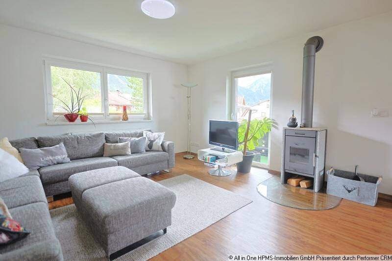 Geräumiges Wohnzimmer mit großem Sofa, Kaminofen und viel natürlichem Licht.