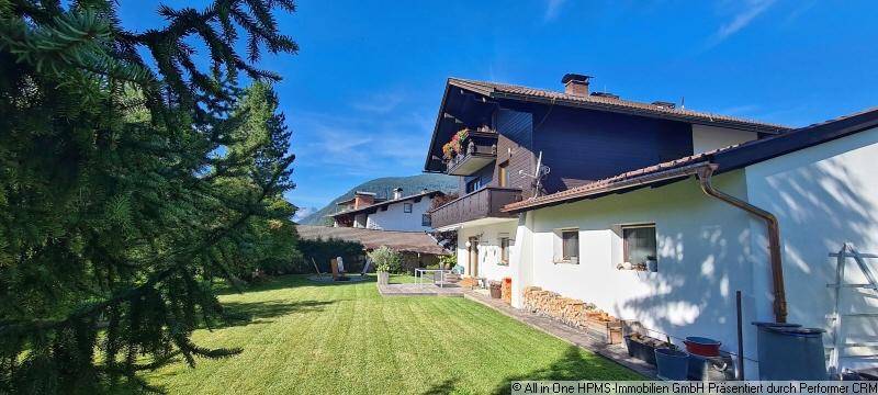 Hausfassade mit gepflegtem Garten, Rasenfläche und Blick auf die umliegende Natur.