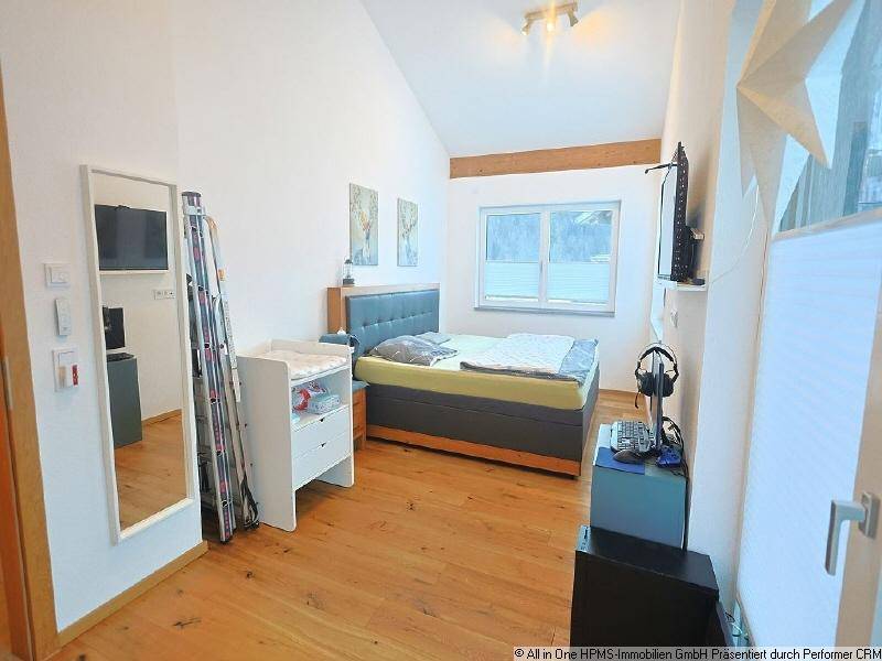 Helles Schlafzimmer mit Holzboden, Dachschräge und Blick auf die verschneite Landschaft.