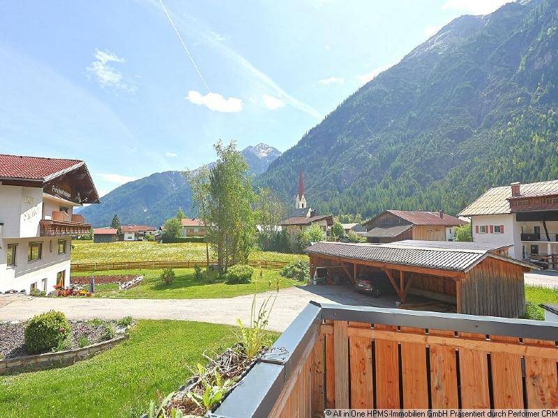 Weitläufiger Blick von der Terrasse auf die Berglandschaft, umliegende Häuser und einen Carport.